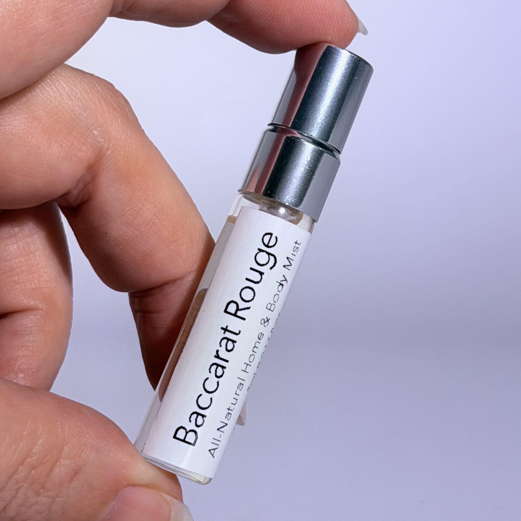 Hand holding a small 5ml clear Baccarat Rouge bottle against a light background