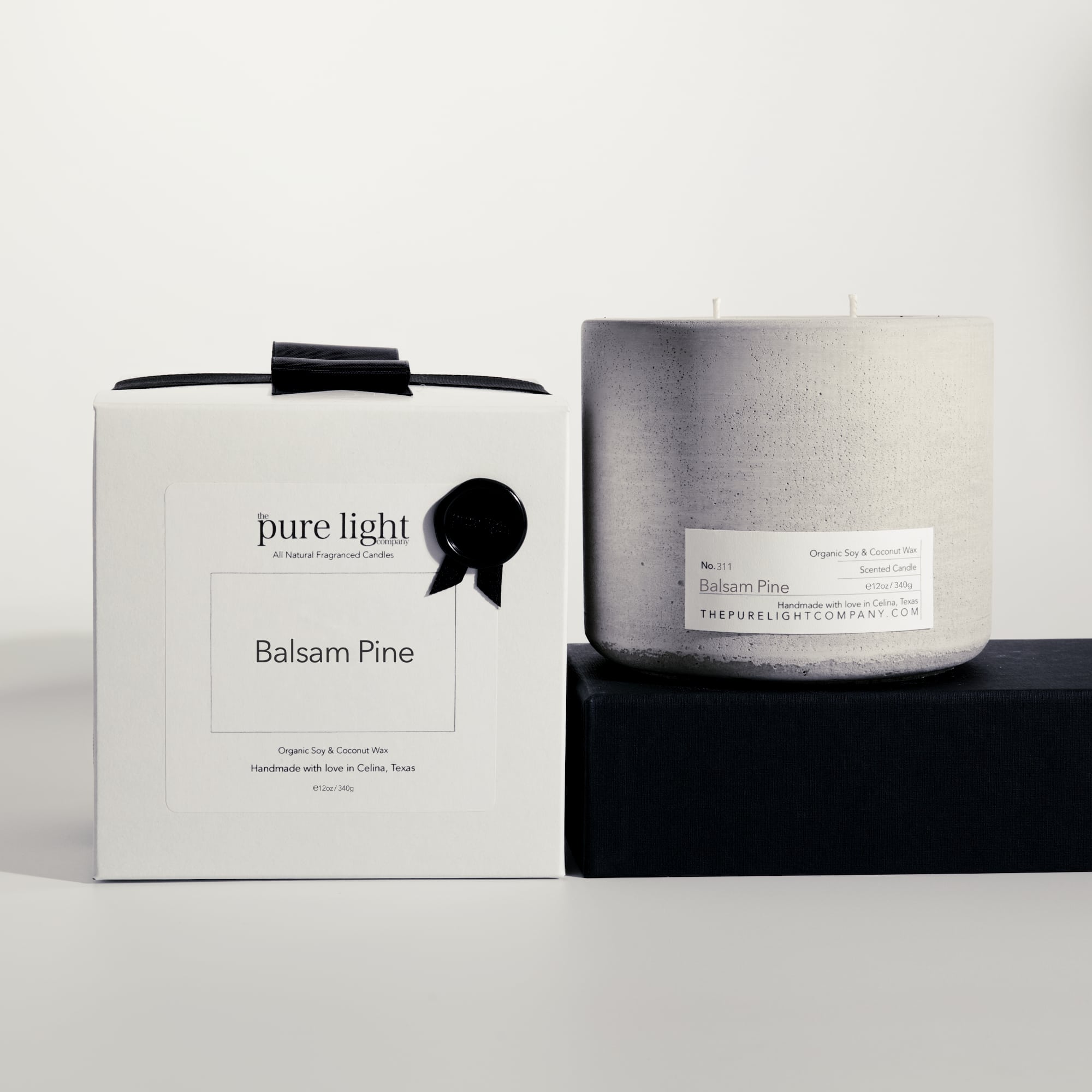 Large Balsam Pine gray concrete candle on a prop beside a gift box with ribbon and wax seal by The Pure Light Company.