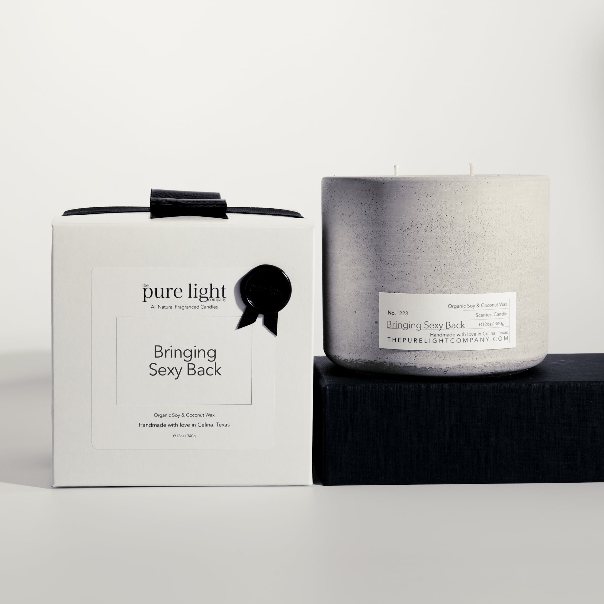 Large Bringing Sexy Back gray concrete candle on a prop beside a gift box with ribbon and wax seal by The Pure Light Company.