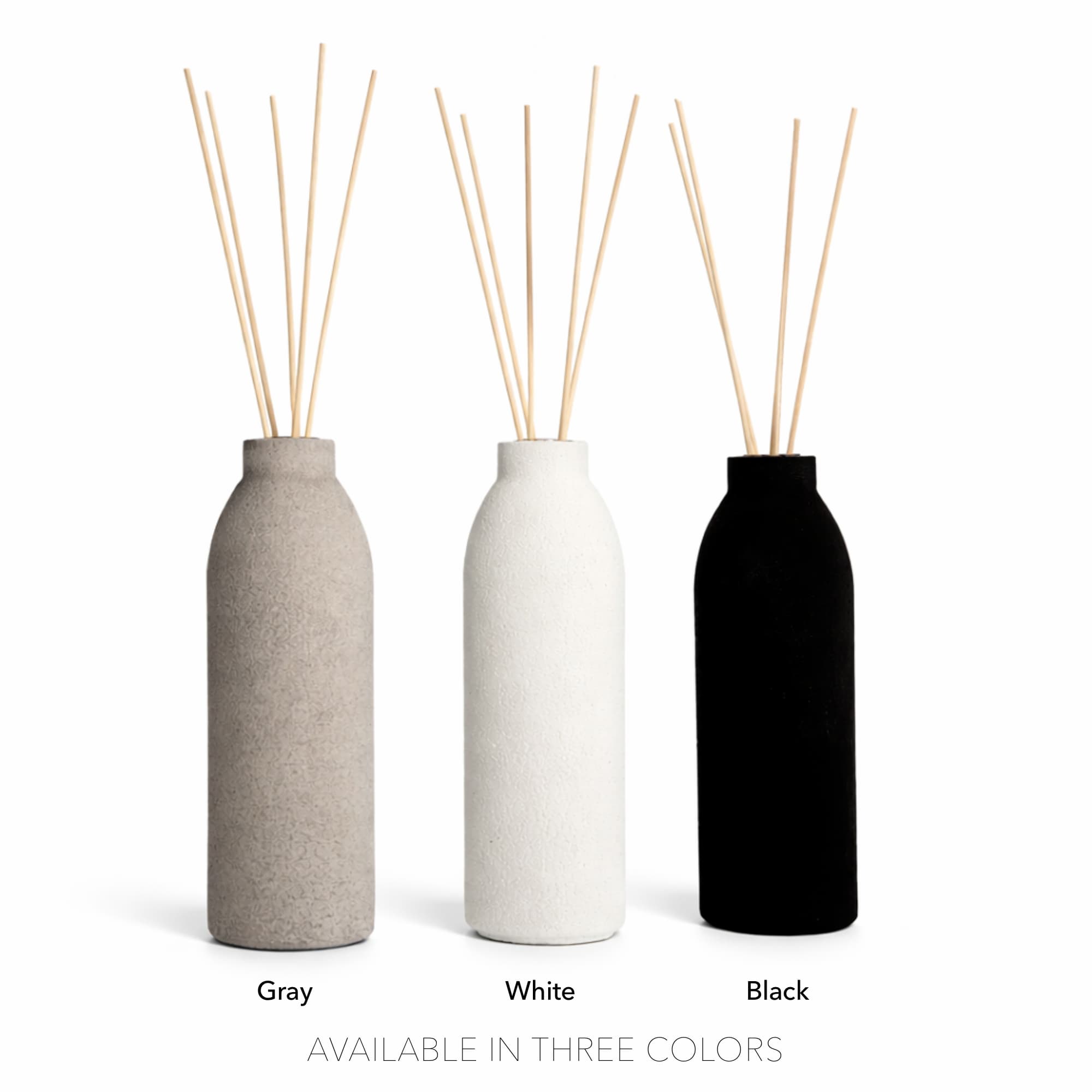 Three Concrete Diffusers by The Pure Light Company in gray, white, and black with wooden sticks on a white background.