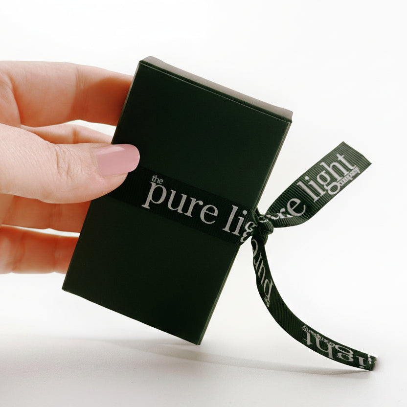 Hand holding a black box with 'the pure light' ribbon on a white background by The Pure Light Company