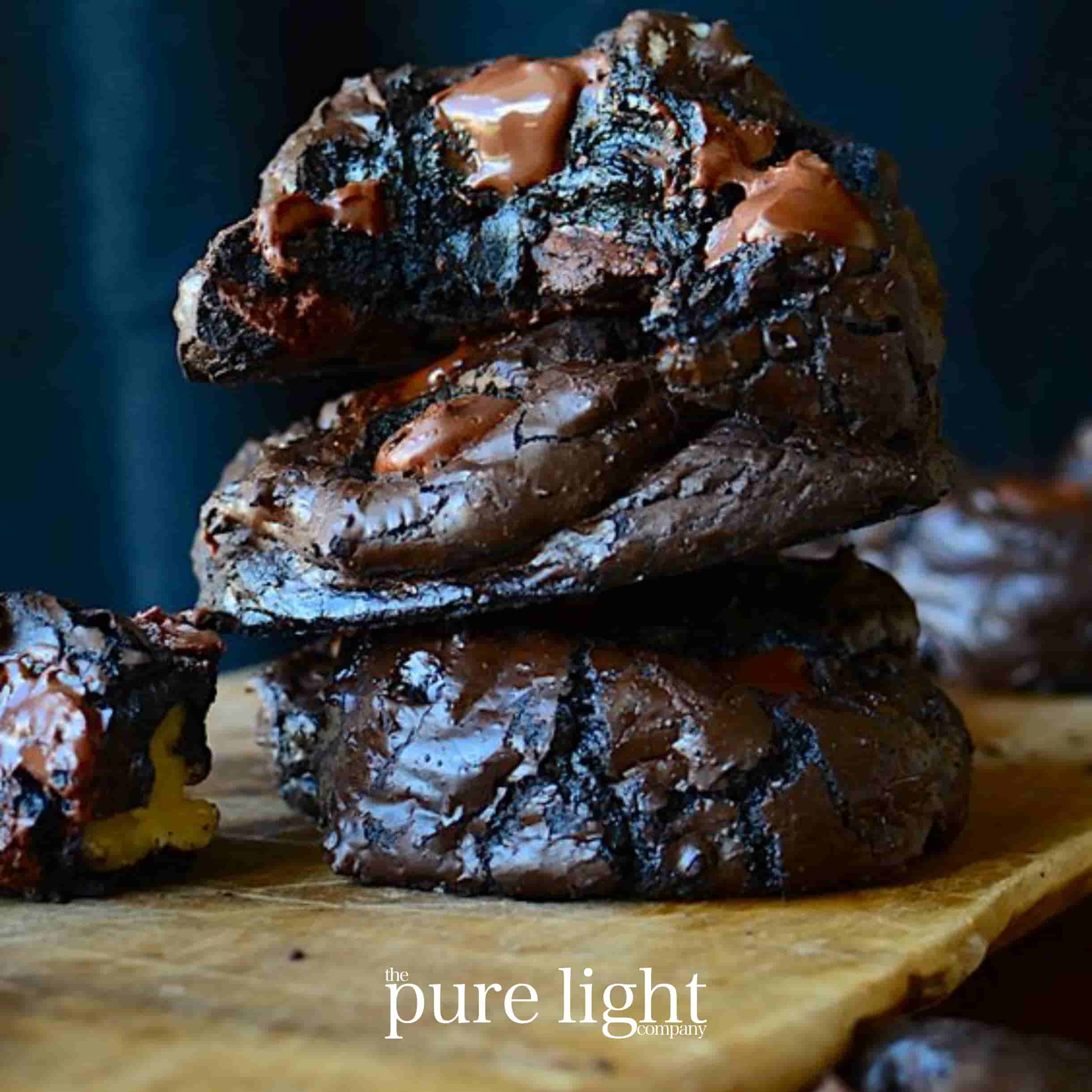 A stack of deliciously rich fudge brownies on a rustic chopping board for the Decadent Fudge Brownie home fragrance collection by The Pure Light Company.