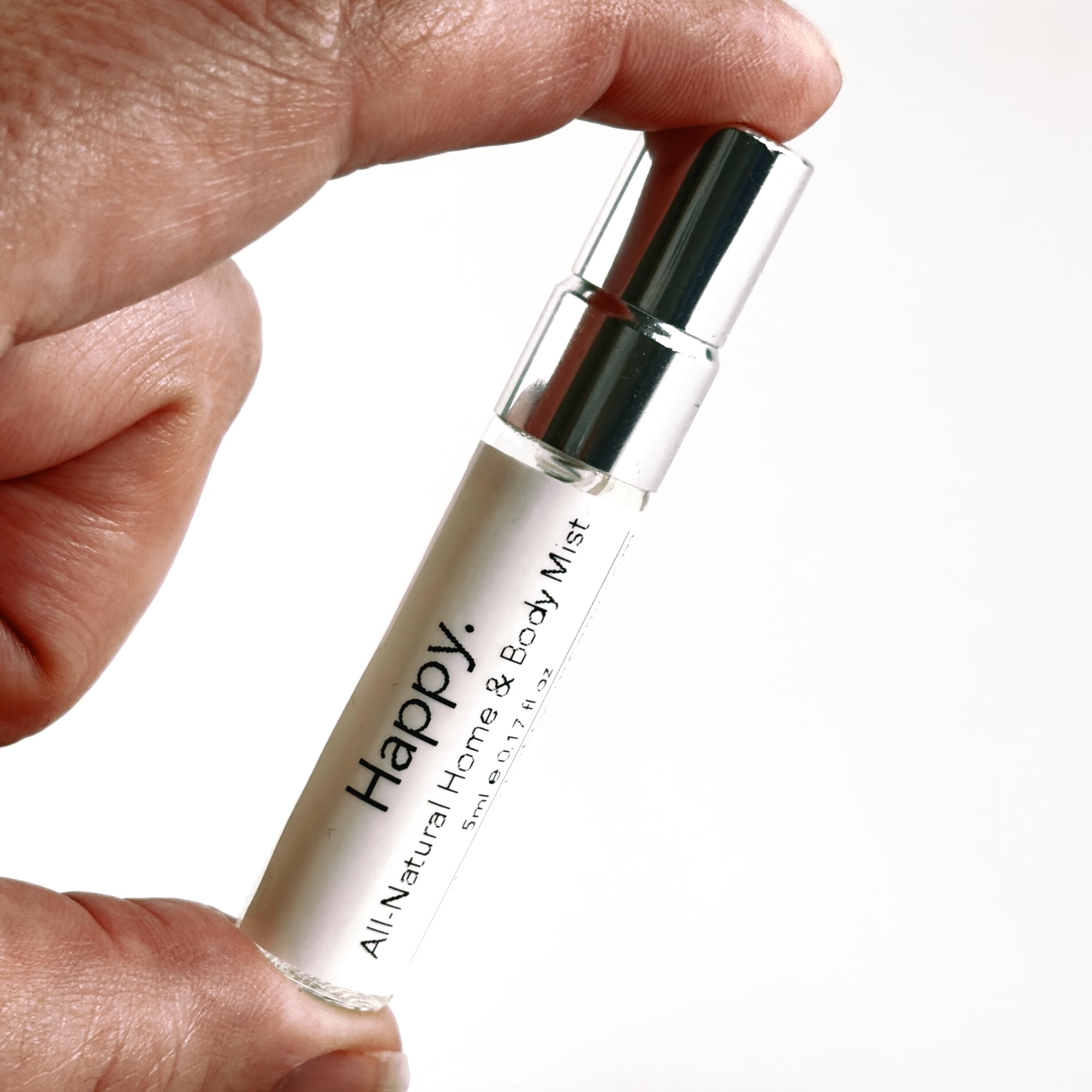 Hand holding a clear bottle labeled 'Happy' with black text on a white background by The Pure Light Company