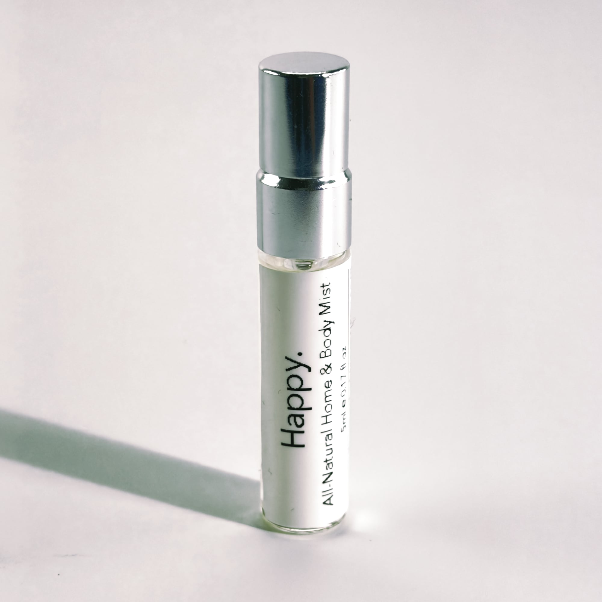 Silver spray bottle of 'Happy' all-natural home and body mist on a light gray background by The Pure Light Company
