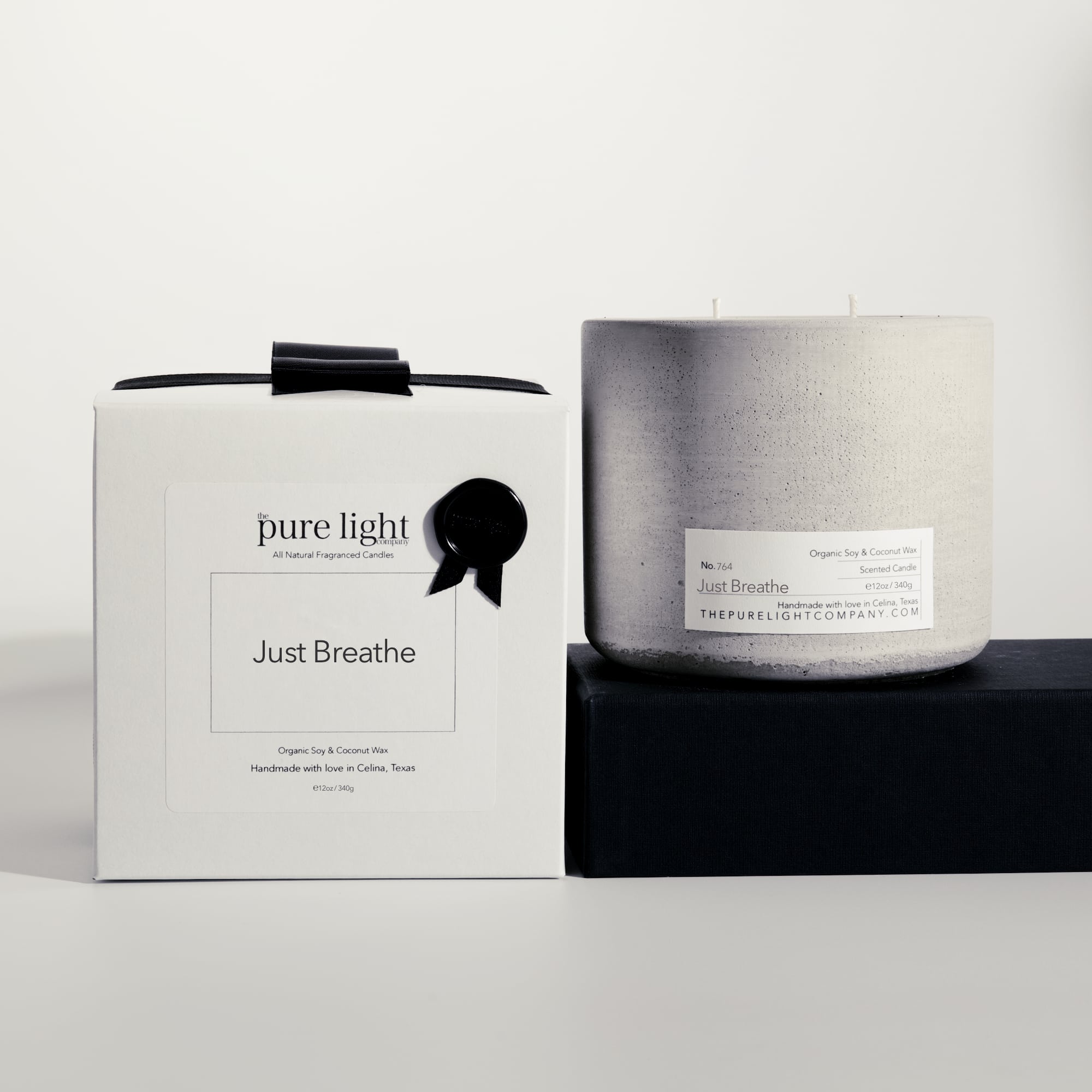 Large Just Breathe gray concrete candle on a prop beside a gift box with ribbon and wax seal by The Pure Light Company.