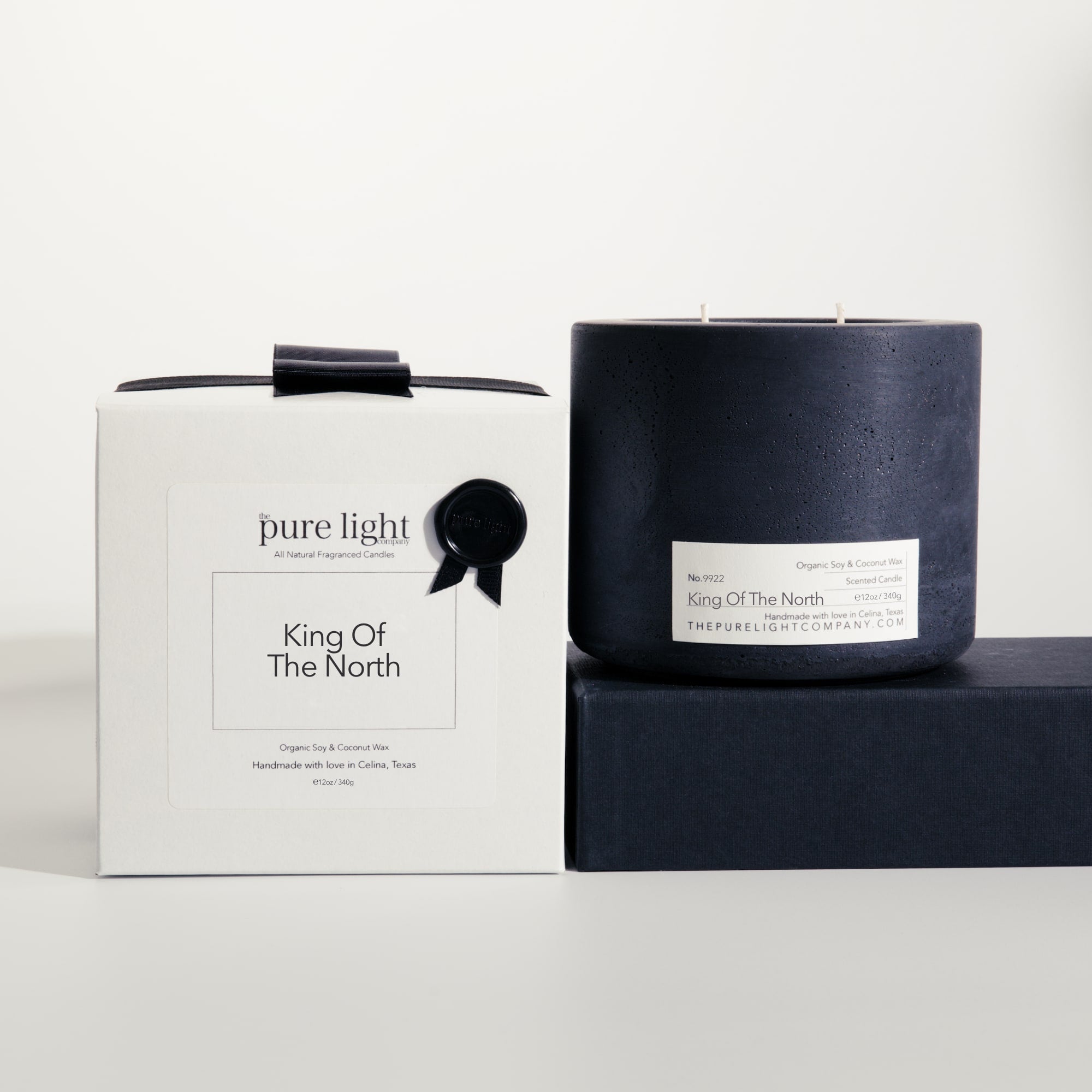 Large King Of The North black concrete candle on a prop beside a gift box with ribbon and wax seal by The Pure Light Company.