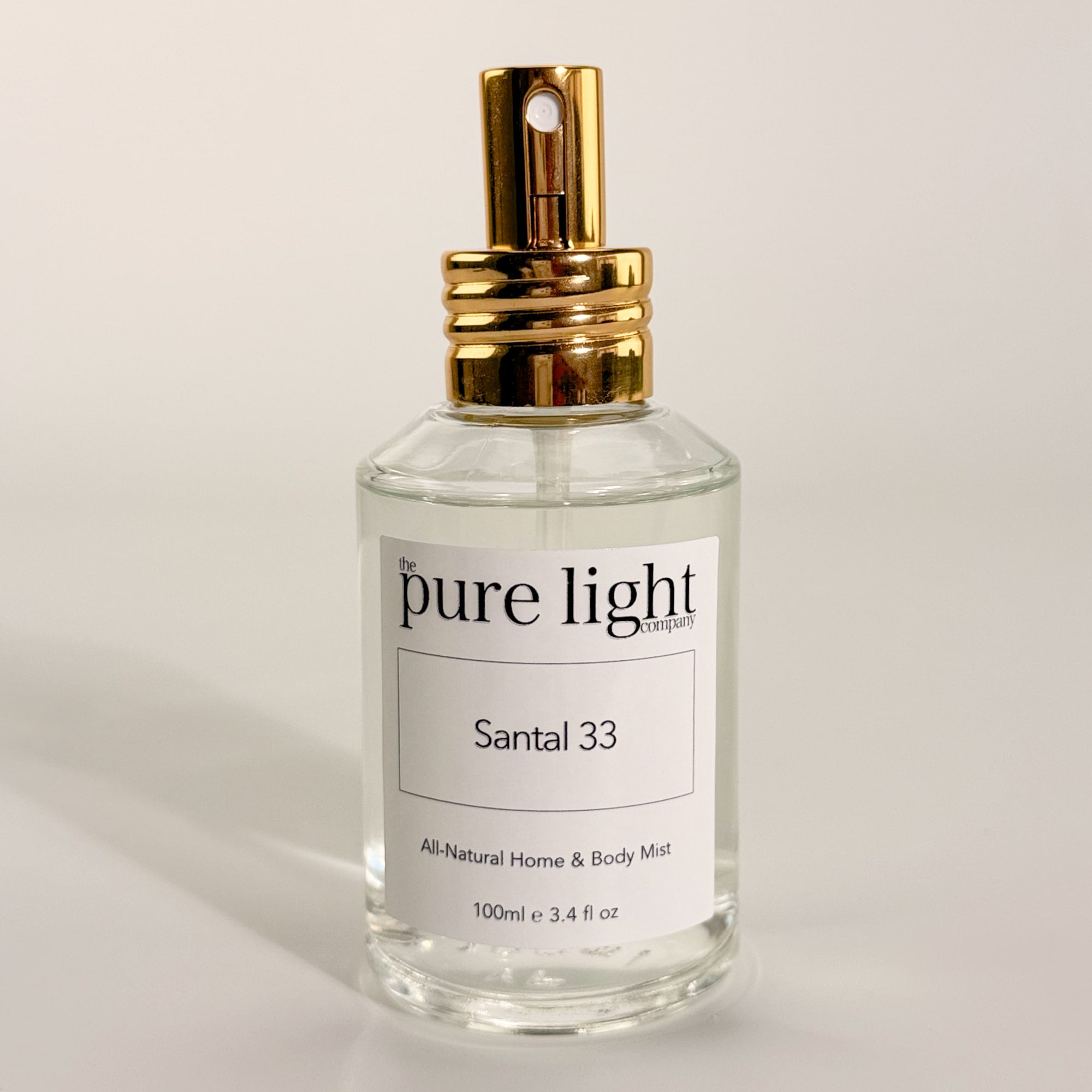 Bottle of The Pure Light Company Santal 33 LeLabo Dupe All-Natural Home and Body Mist 100ml clear glass bottle with a gold cap on a white background