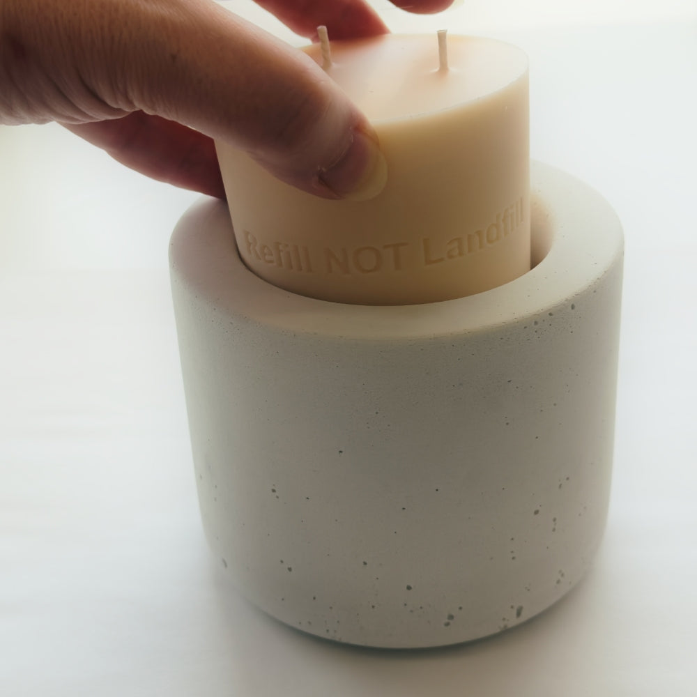 Hand placing a refill candle into a concrete holder with 'Refill NOT Landfill' text by The Pure Light Company.