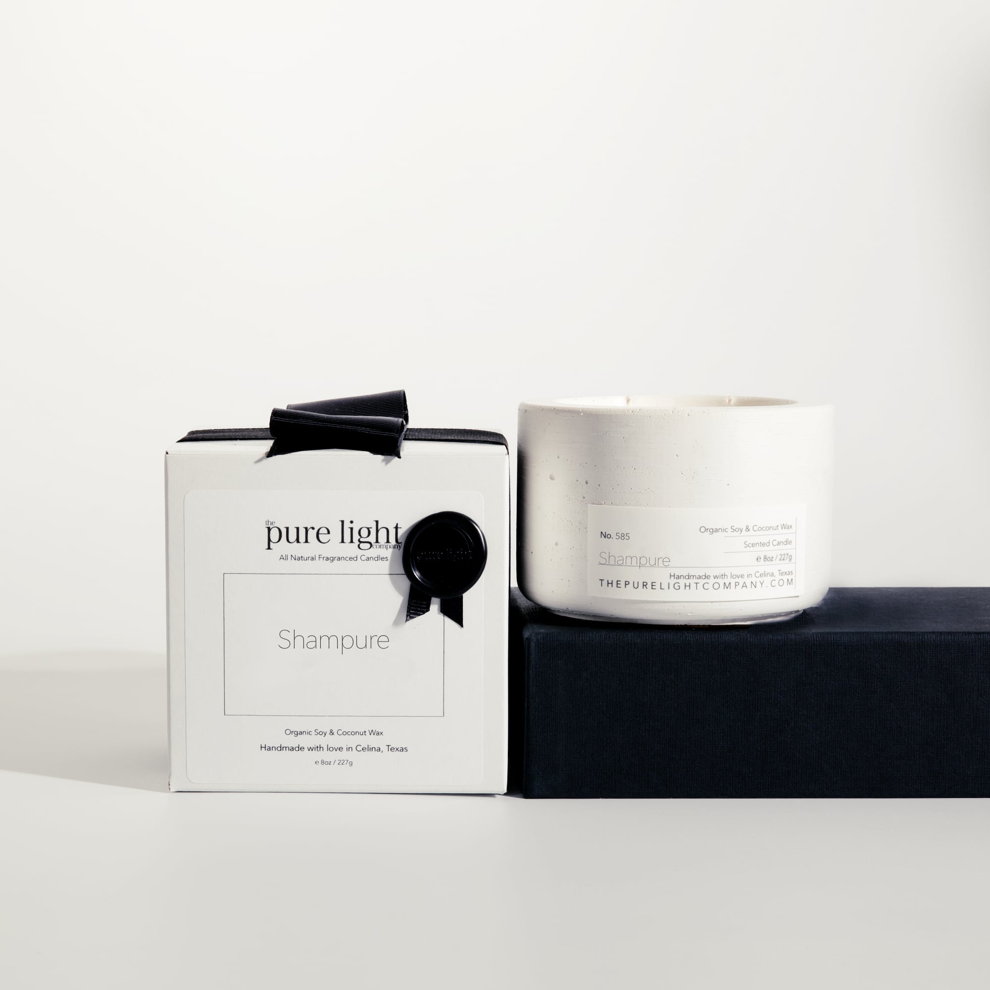 Medium Shampure Aveda Dupe white concrete candle on a prop beside a gift box with ribbon and wax seal by The Pure Light Company