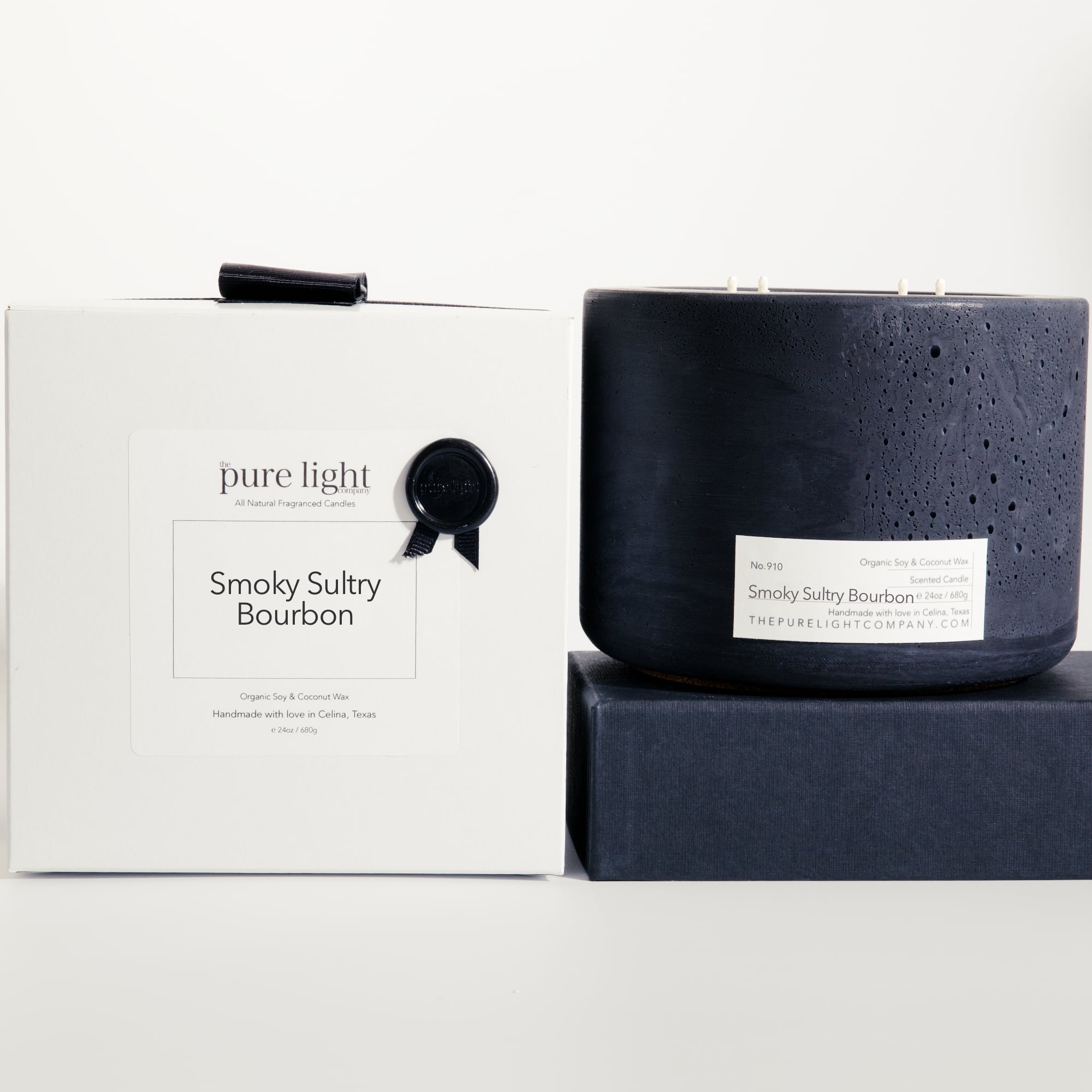 Extra large Smoky Sultry Bourbon black concrete candle on a prop beside a gift box with ribbon and wax seal by The Pure Light Company.