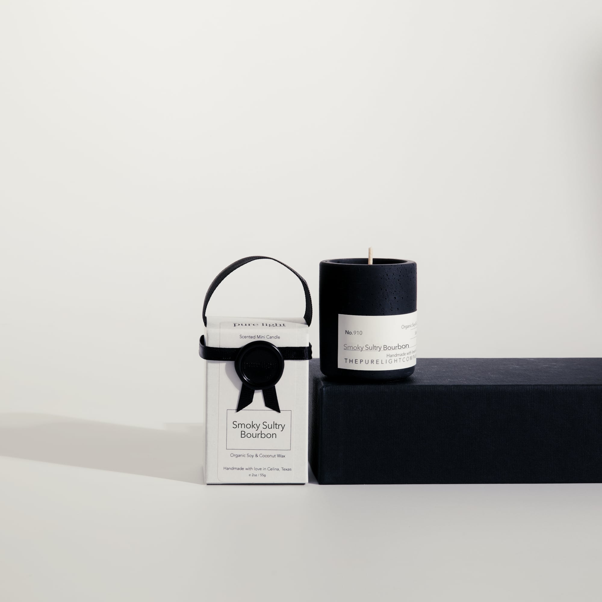 Mini Smoky Sultry Bourbon concrete candle on a prop beside a gift box with ribbon and wax seal by The Pure Light Company.