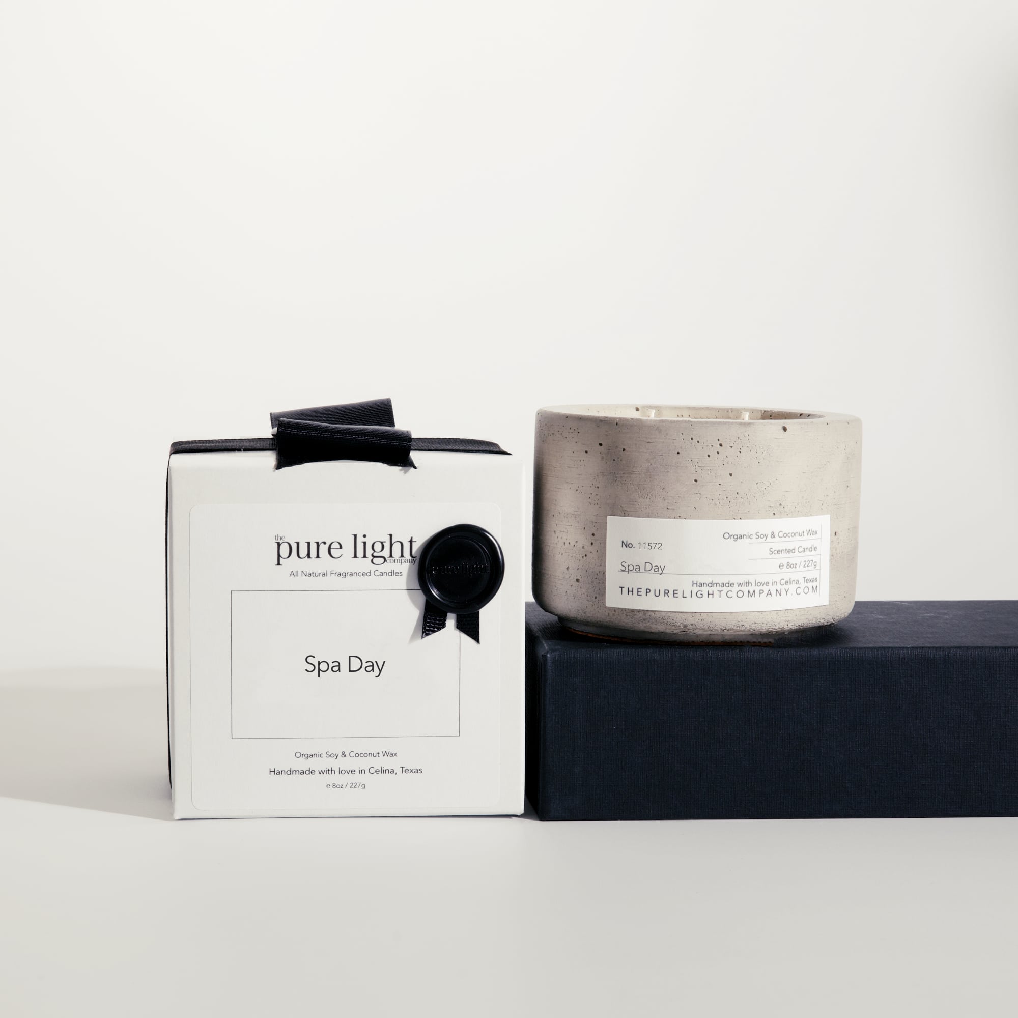 Medium Spa Day gray concrete candle on a prop beside a gift box with ribbon and wax seal by The Pure Light Company.