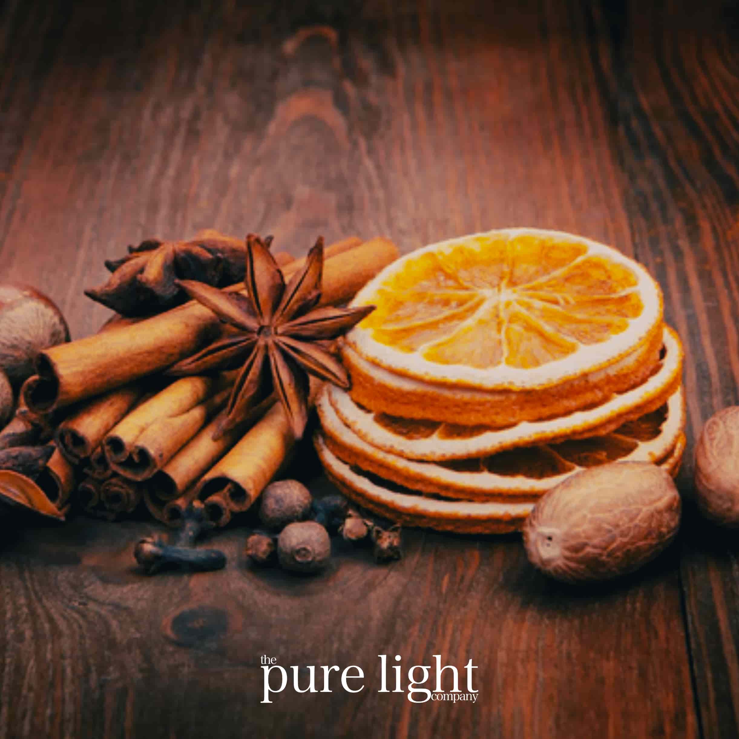 Spices and dried oranges on a wooden surface with The Pure Light Company branding.