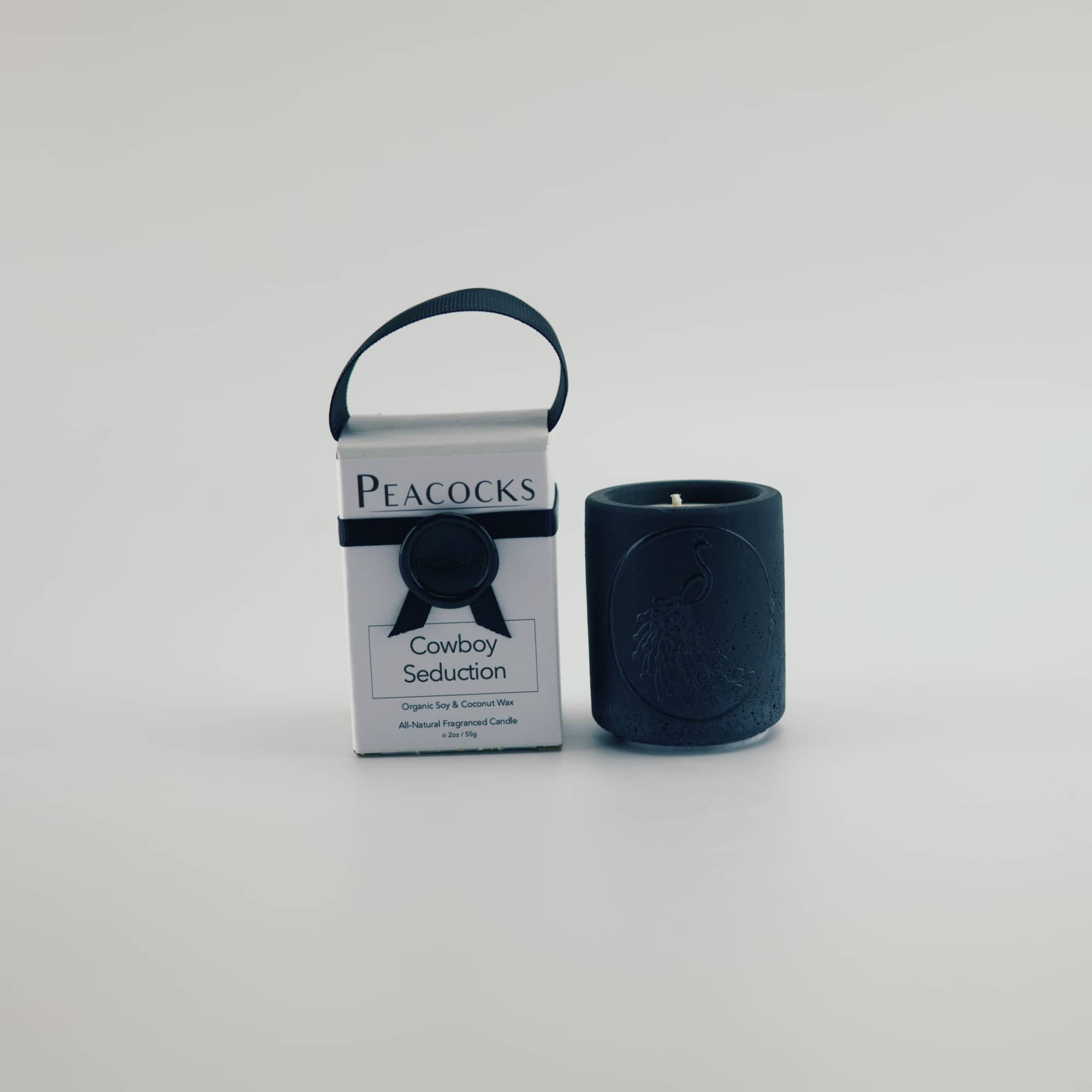Black candle and packaging labeled 'Peacocks' on a light gray background