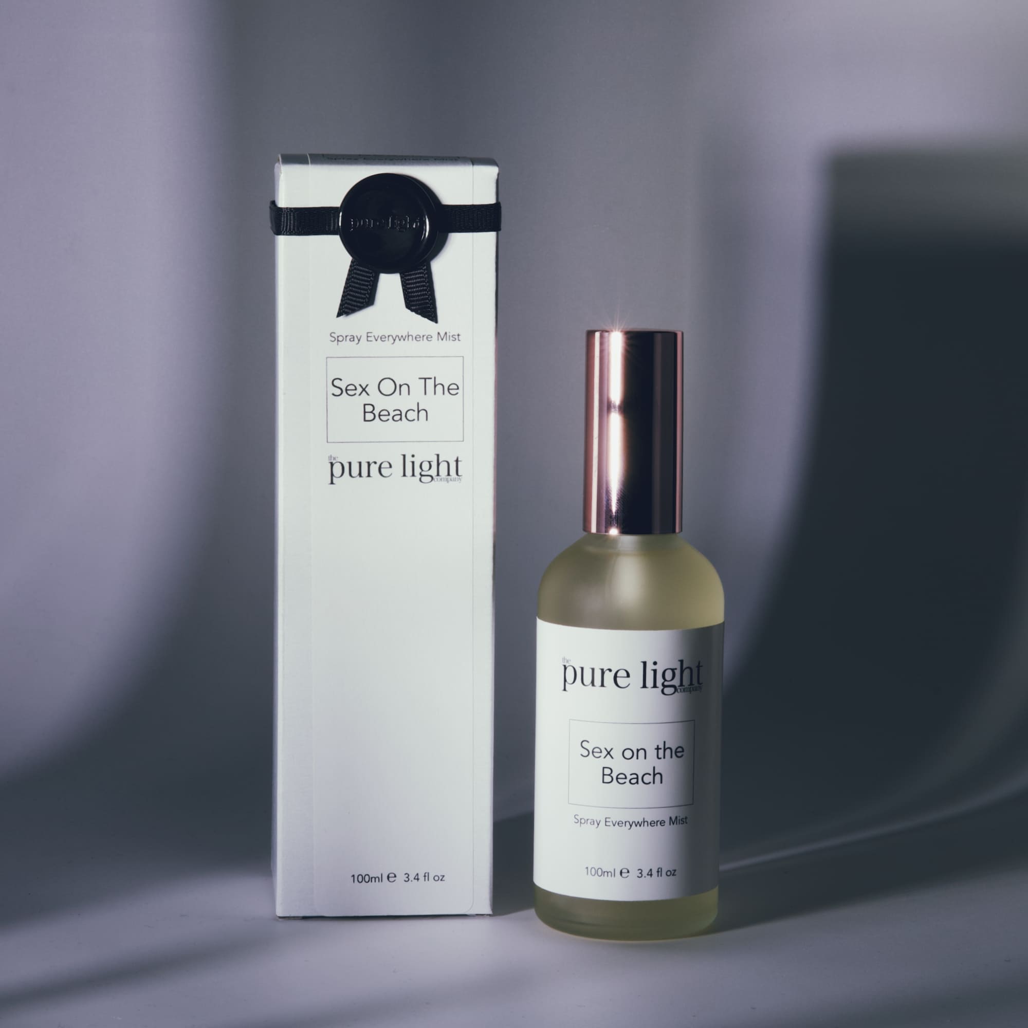 A product image featuring a bottle of "Sex On The Beach" home and body mist with a cap, alongside its packaging box. The cologne bottle is clear with a white label and the cap is metallic rose gold.