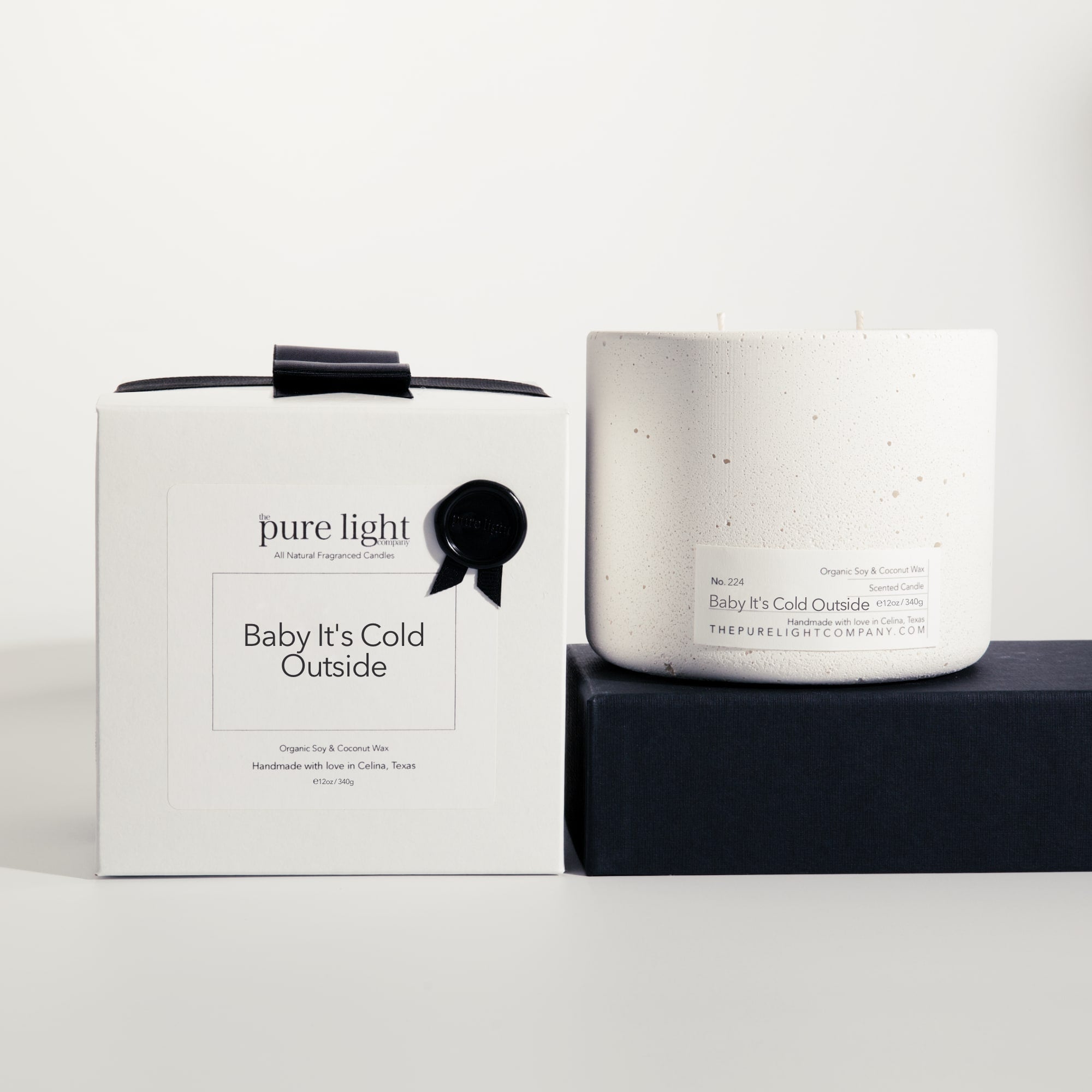 Large Baby It's Cold Outside white concrete candle on a prop beside a gift box with ribbon and wax seal by The Pure Light Company