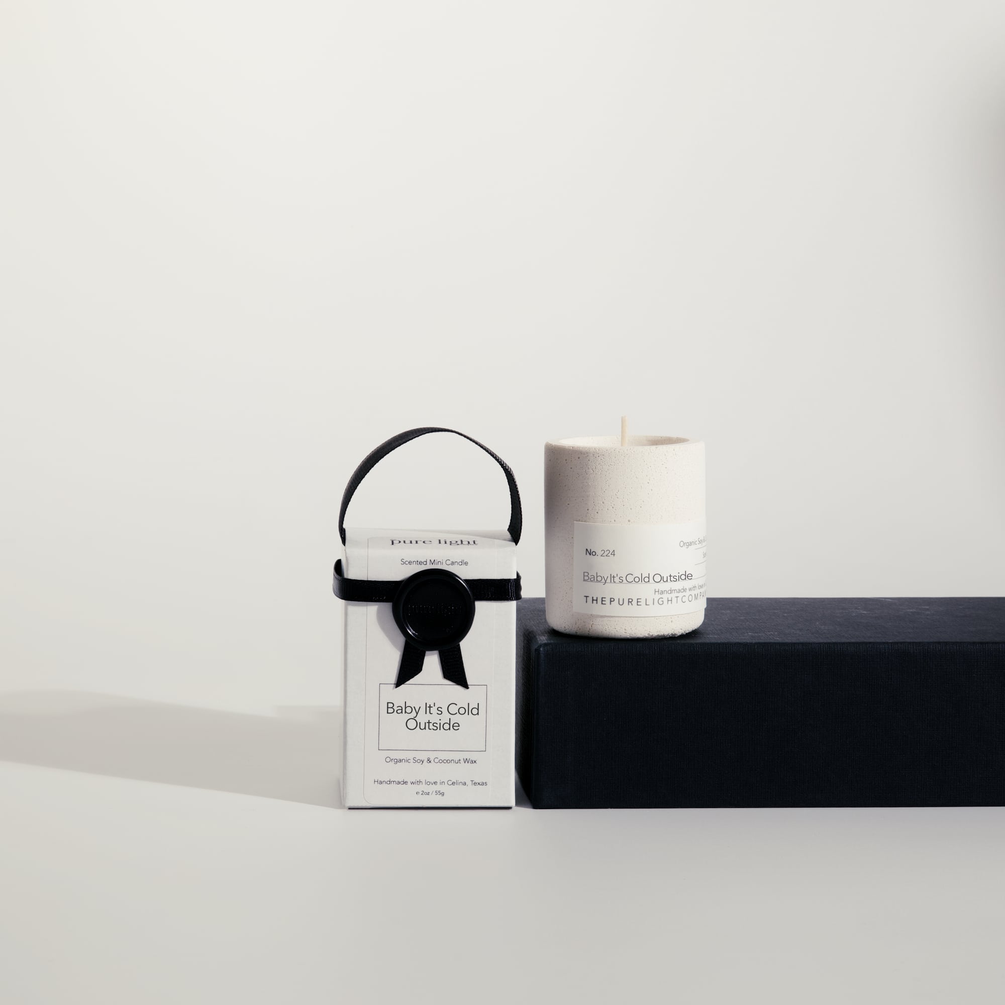 Mini Baby It's Cold Outside concrete candle on a prop beside a gift box with ribbon and wax seal by The Pure Light Company.