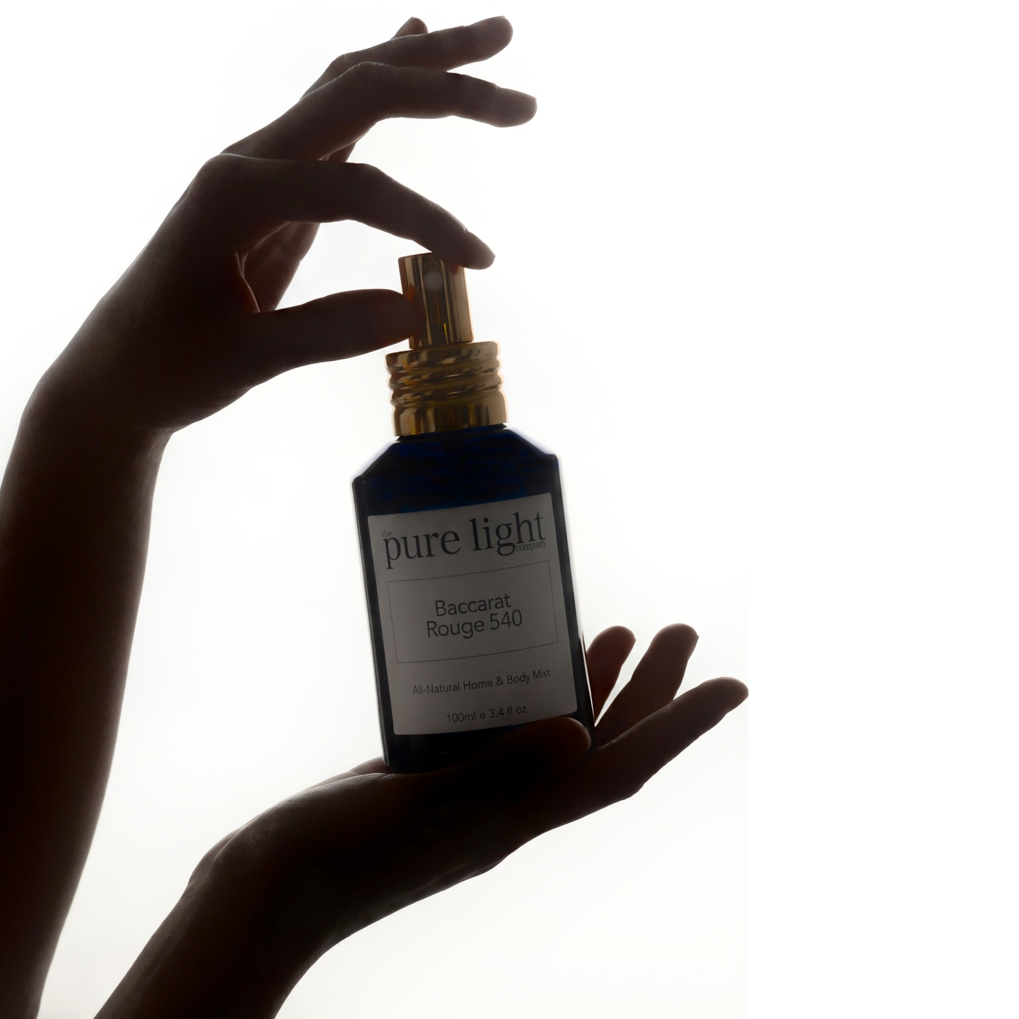 Silhouette of a hand holding a bottle of Baccarat Rouge 540 All-Natural Home & Body Mist by The Pure Light Company against a white background
