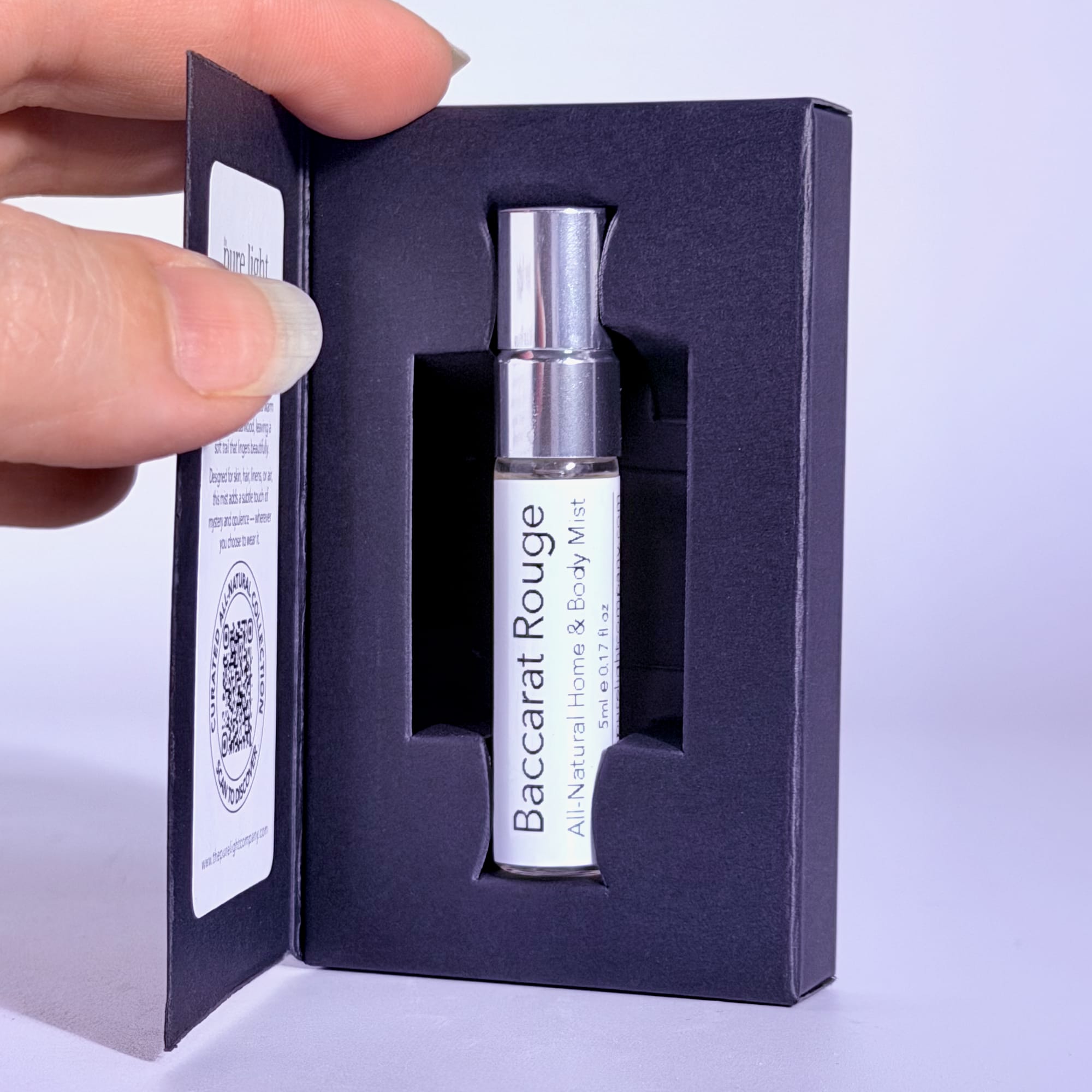 Baccarat Rouge perfume bottle in a black box held by a hand on a white background.