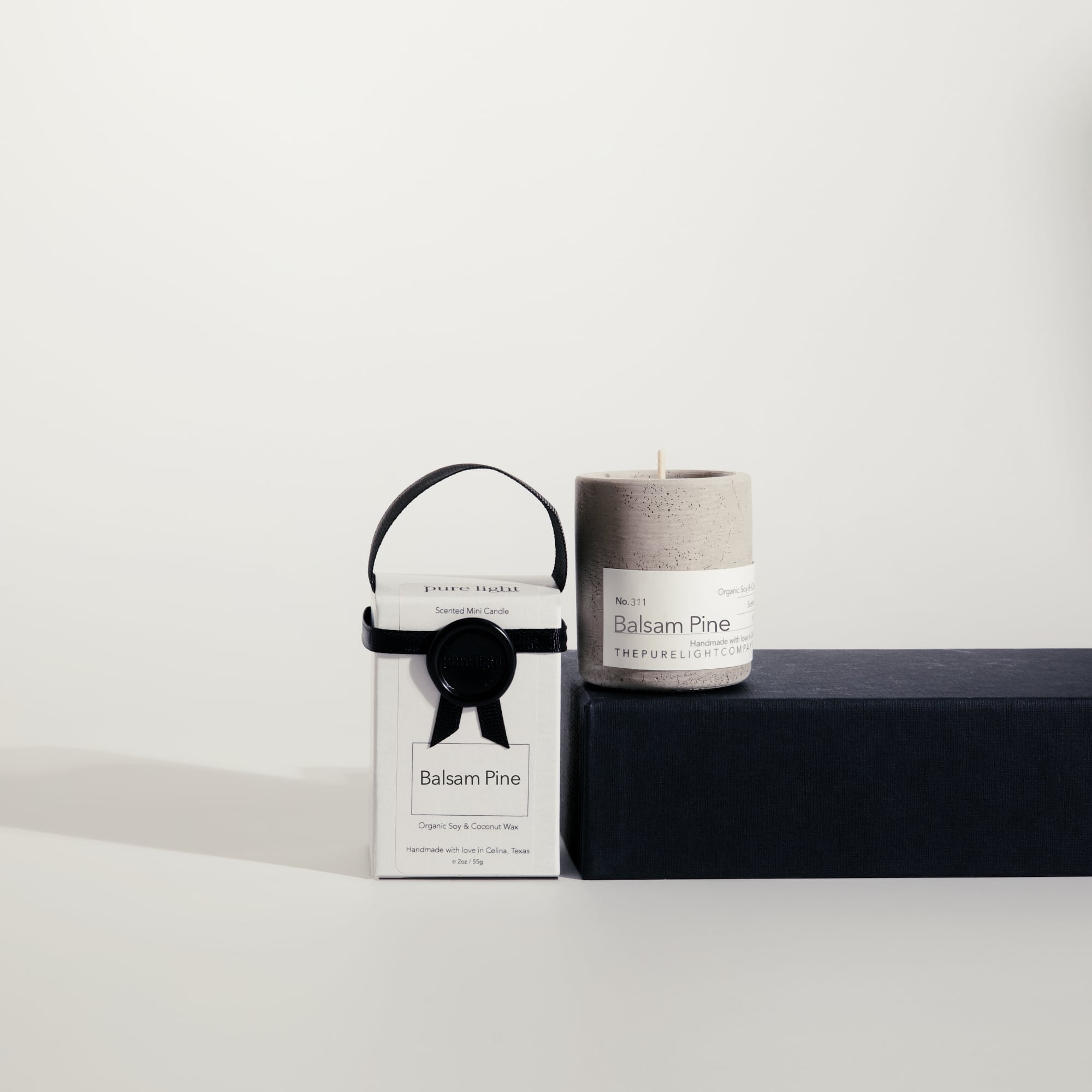 Mini Balsam Pine concrete candle on a prop beside a gift box with ribbon and wax seal by The Pure Light Company.