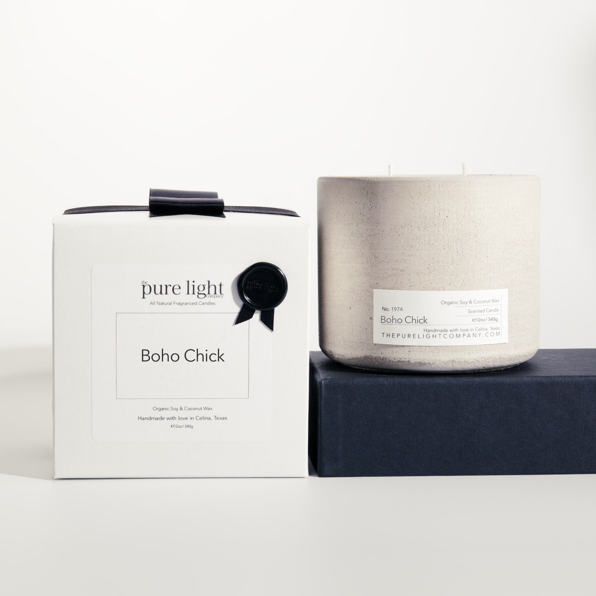 Large Boho Chick gray concrete candle on a prop beside a gift box with ribbon and wax seal by The Pure Light Company.