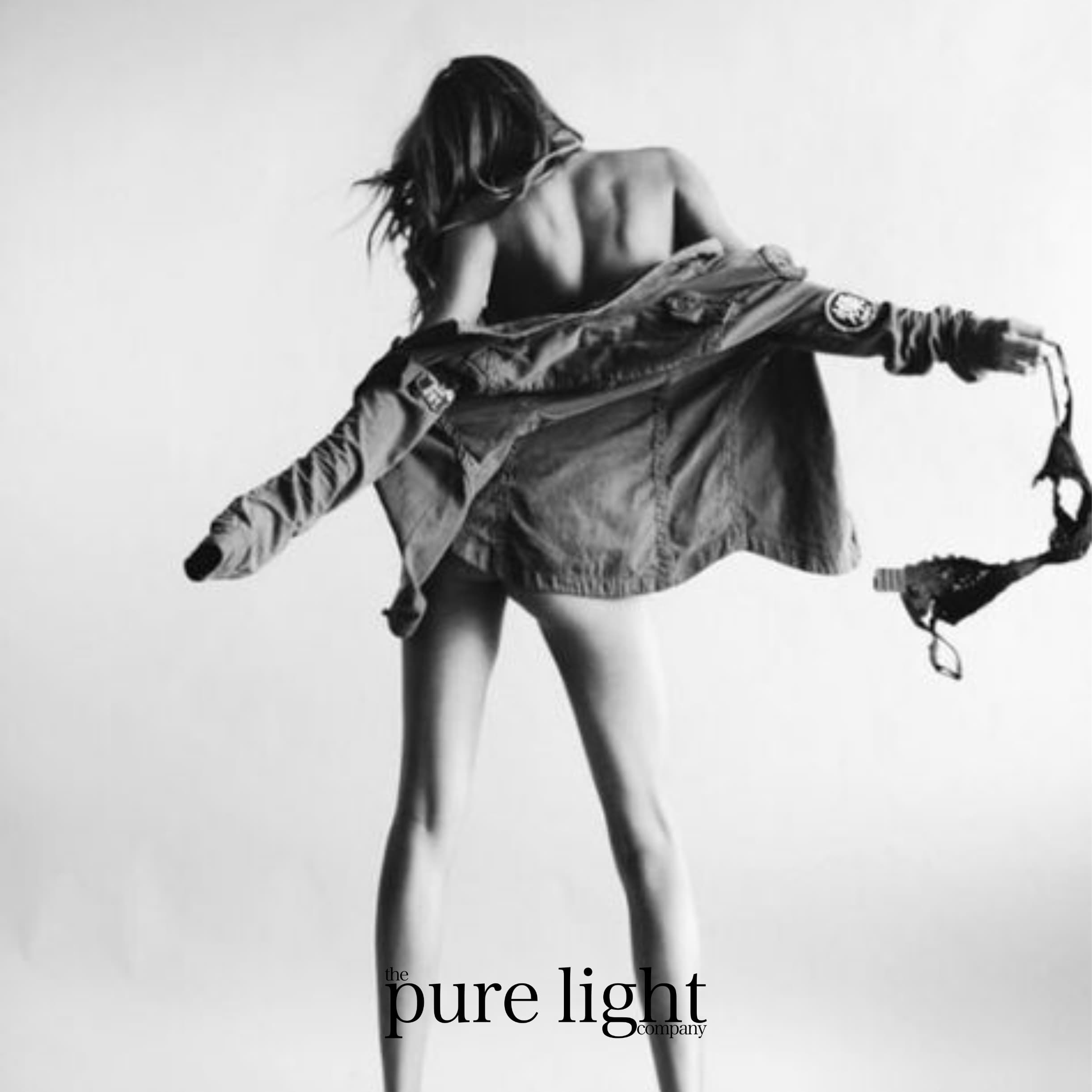 Black and white image of attractive female dancing with her underwear in her hands with The Pure Light Logo.