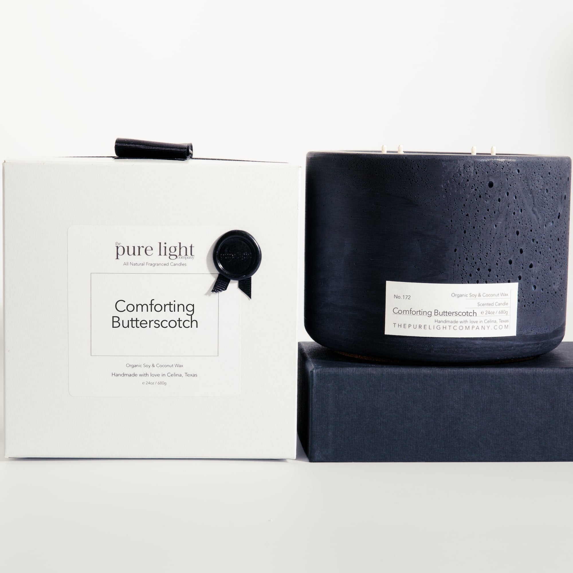 Extra large Comforting Butterscotch black concrete candle on a prop beside a gift box with ribbon and wax seal by The Pure Light Company.