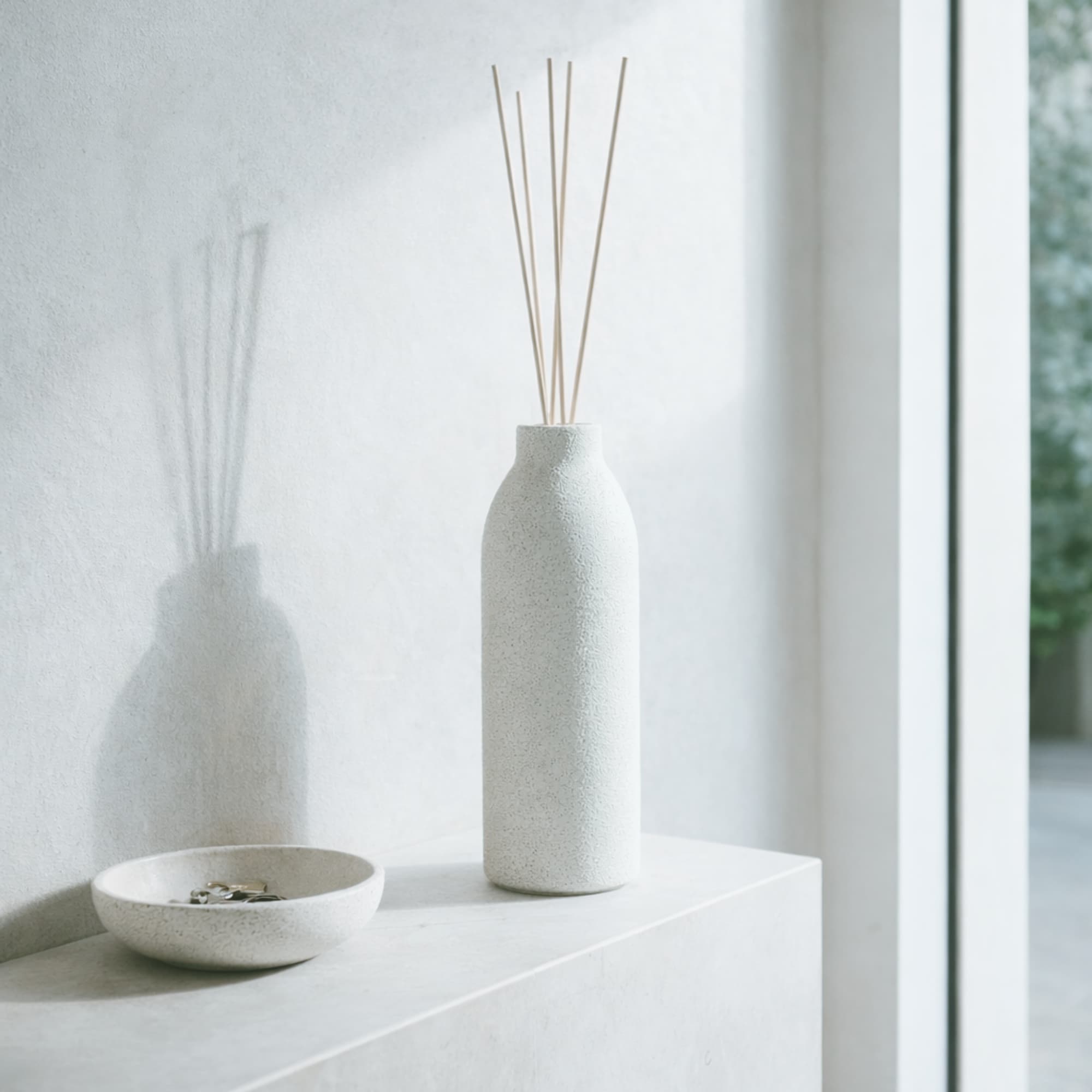 White concrere diffuser with natural colored reeds on a white surface near a window