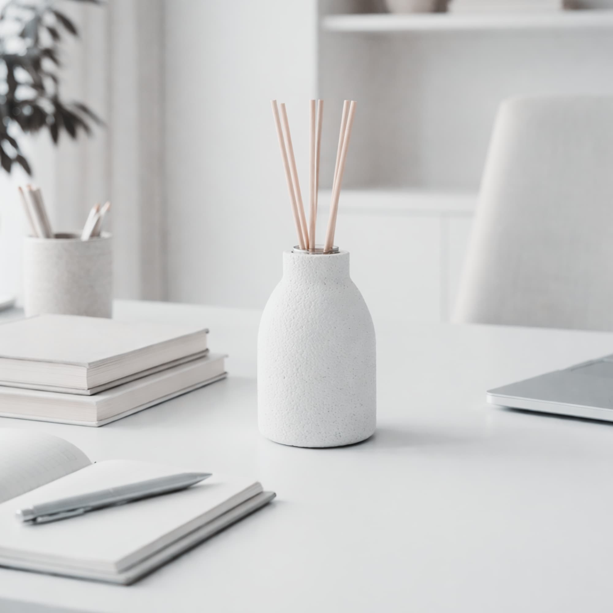 White concrete diffuser with natural reeds on a desk with books and a laptop in a minimalistic office setting
