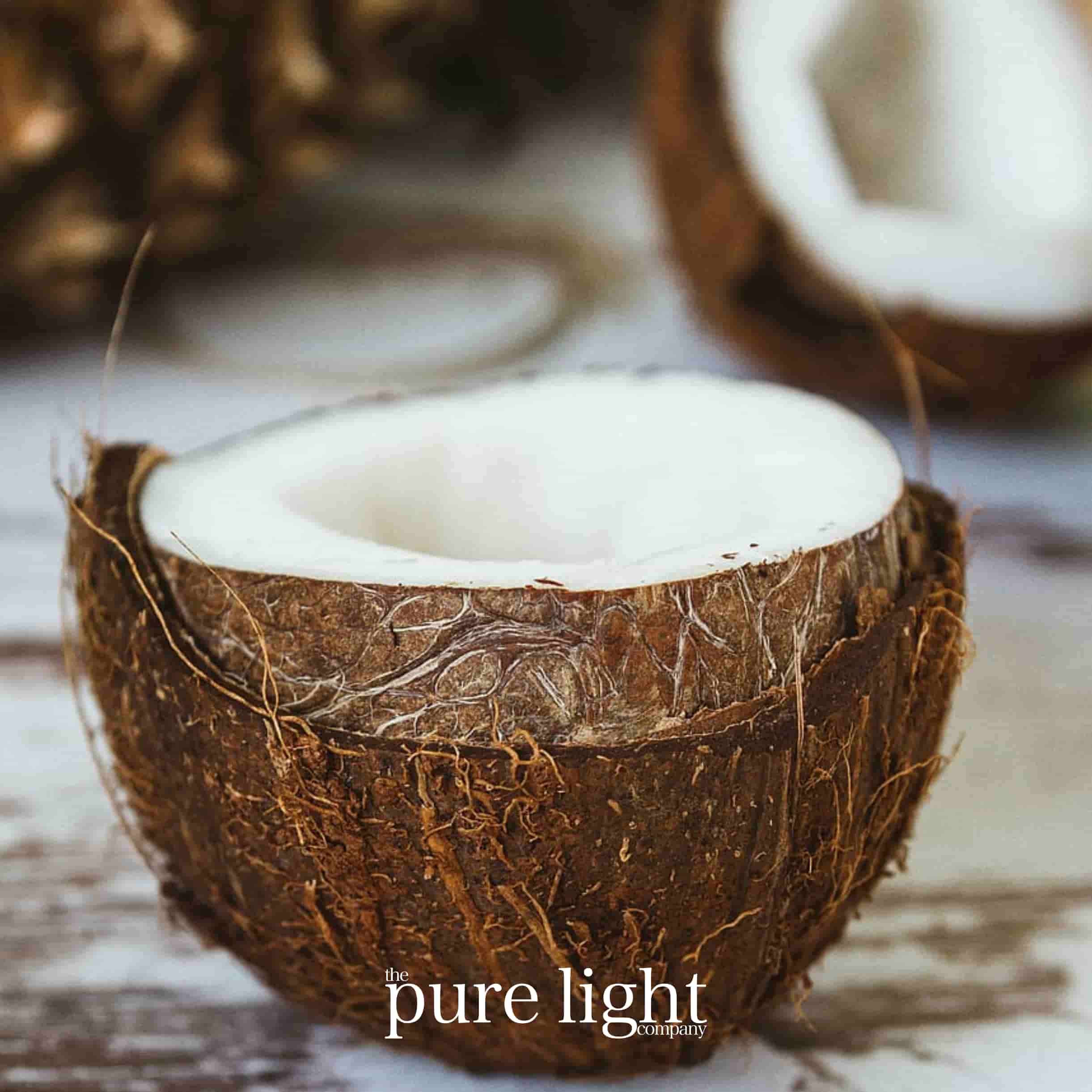 A fresh creamy coconut cut in half, lying on a sandy beach with The Pure Light Company logo