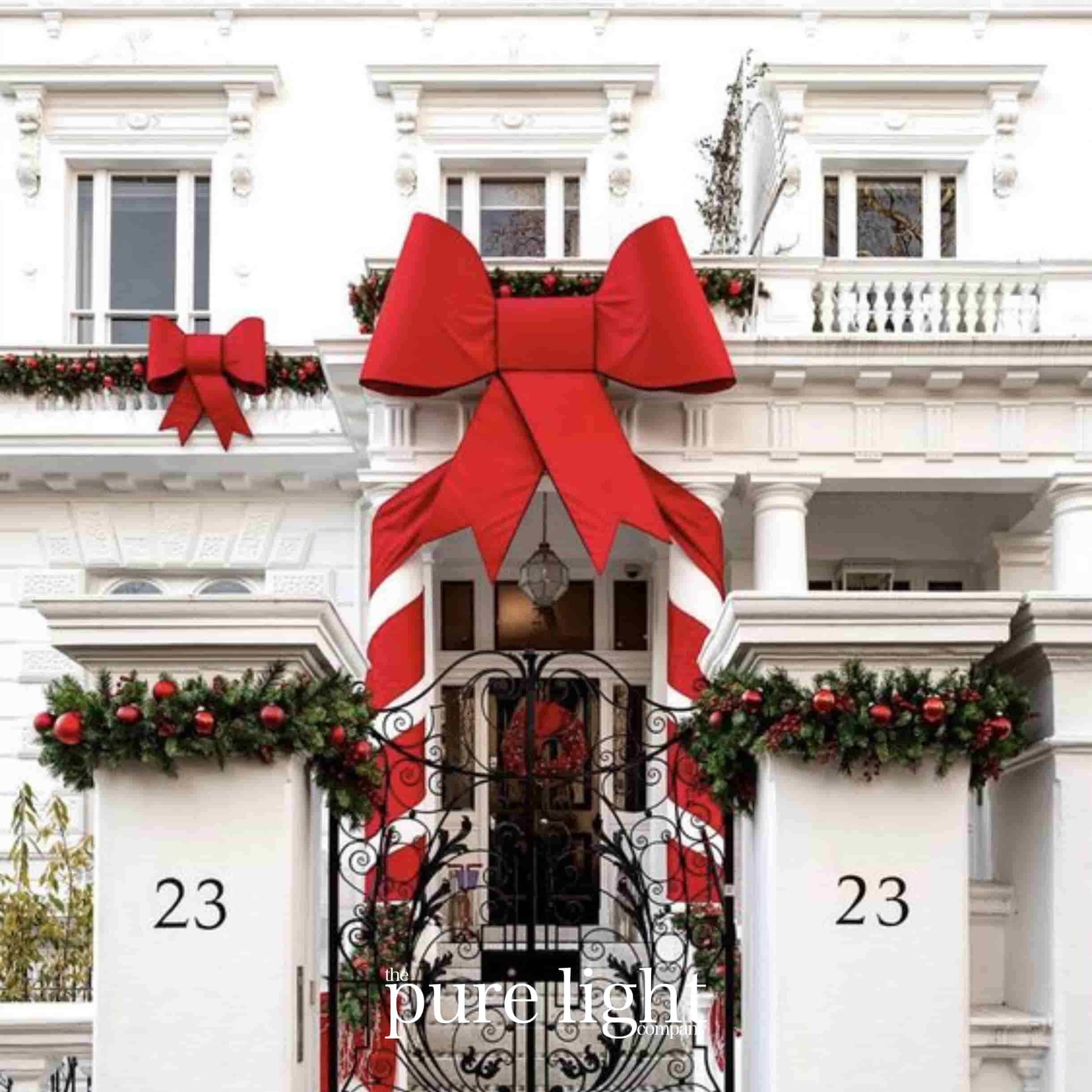 Decorative red bow and Christmas garlands on a building facade with The Pure Light Company logo