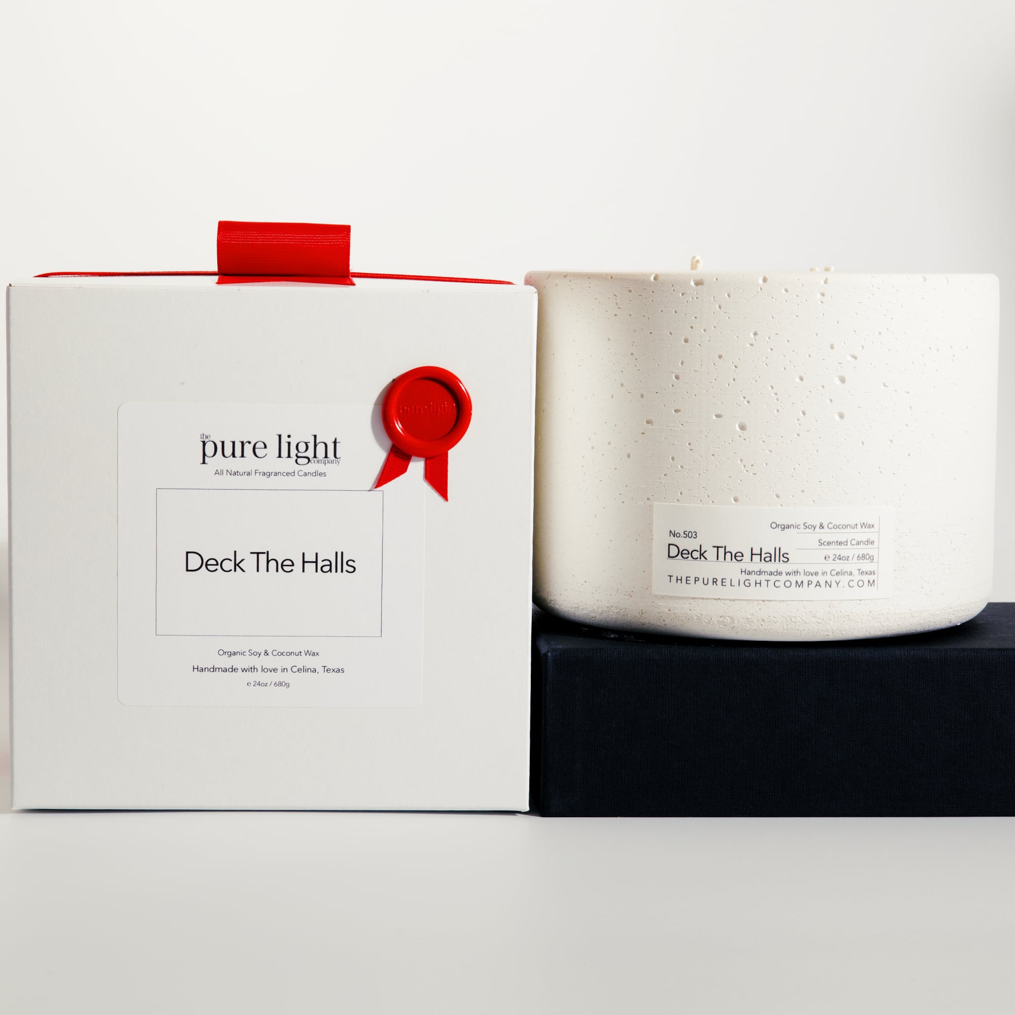 Extra Large Deck The Halls white concrete candle on a prop beside a gift box with ribbon and wax seal by The Pure Light Company.