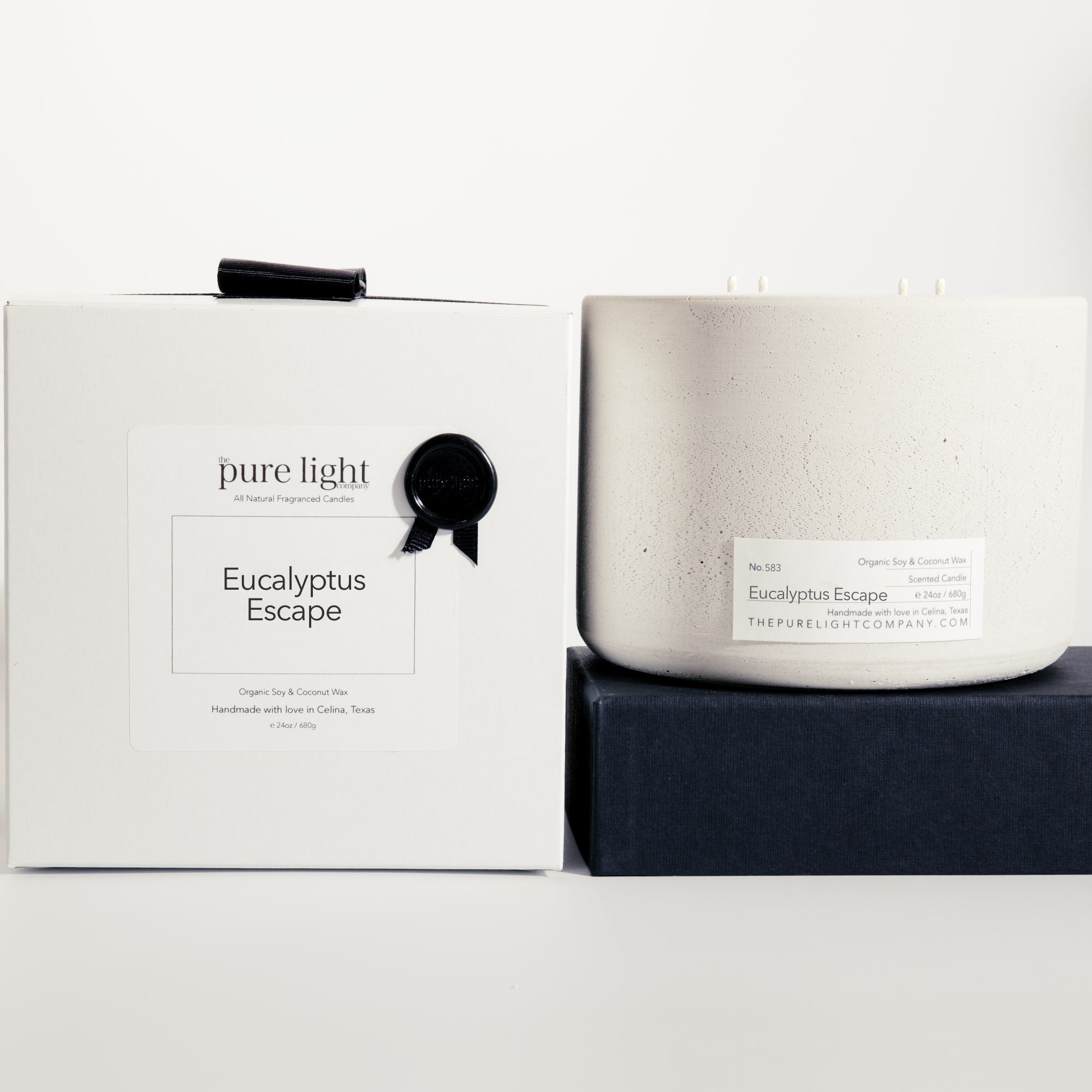 Extra large Eucalyptus Escape gray concrete candle on a prop beside a gift box with ribbon and wax seal by The Pure Light Company.