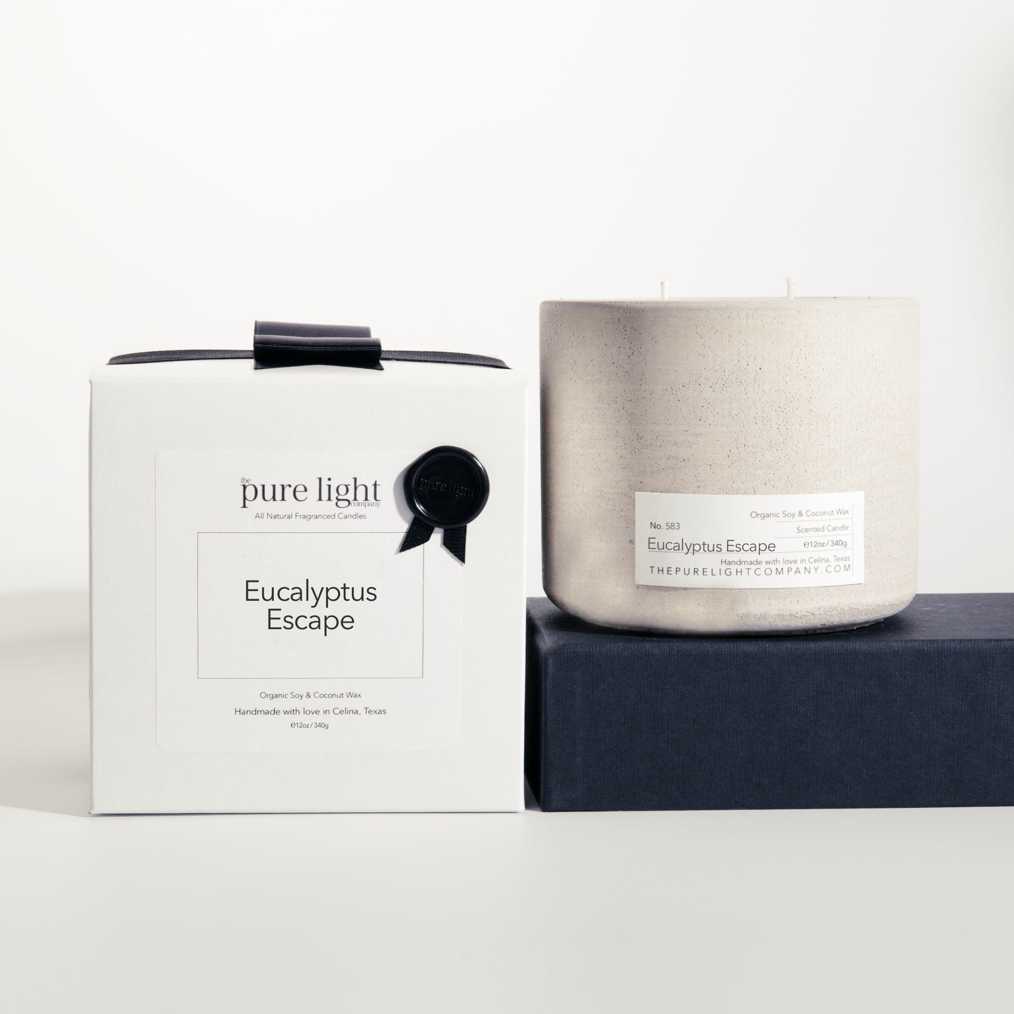 Large Eucalyptus Escape gray concrete candle on a prop beside a gift box with ribbon and wax seal by The Pure Light Company.