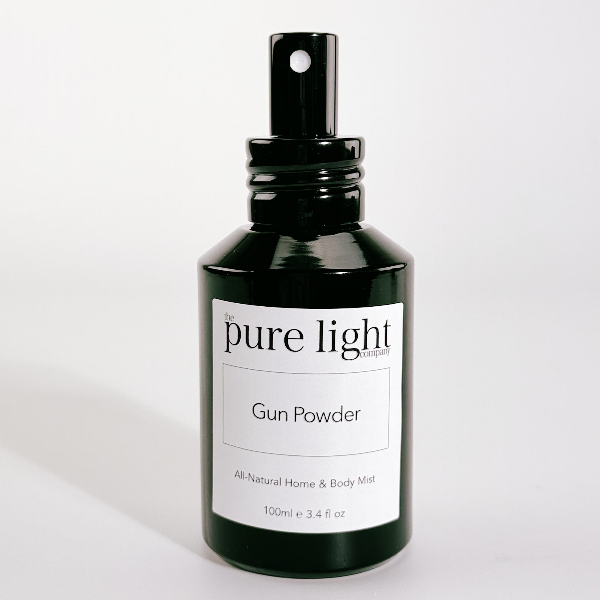 A bottle of The Pure Light Company "Gun Powder" All-Natural Home and Body Mist 100ml glossy black glass bottle with a black metal spray cap on a white background