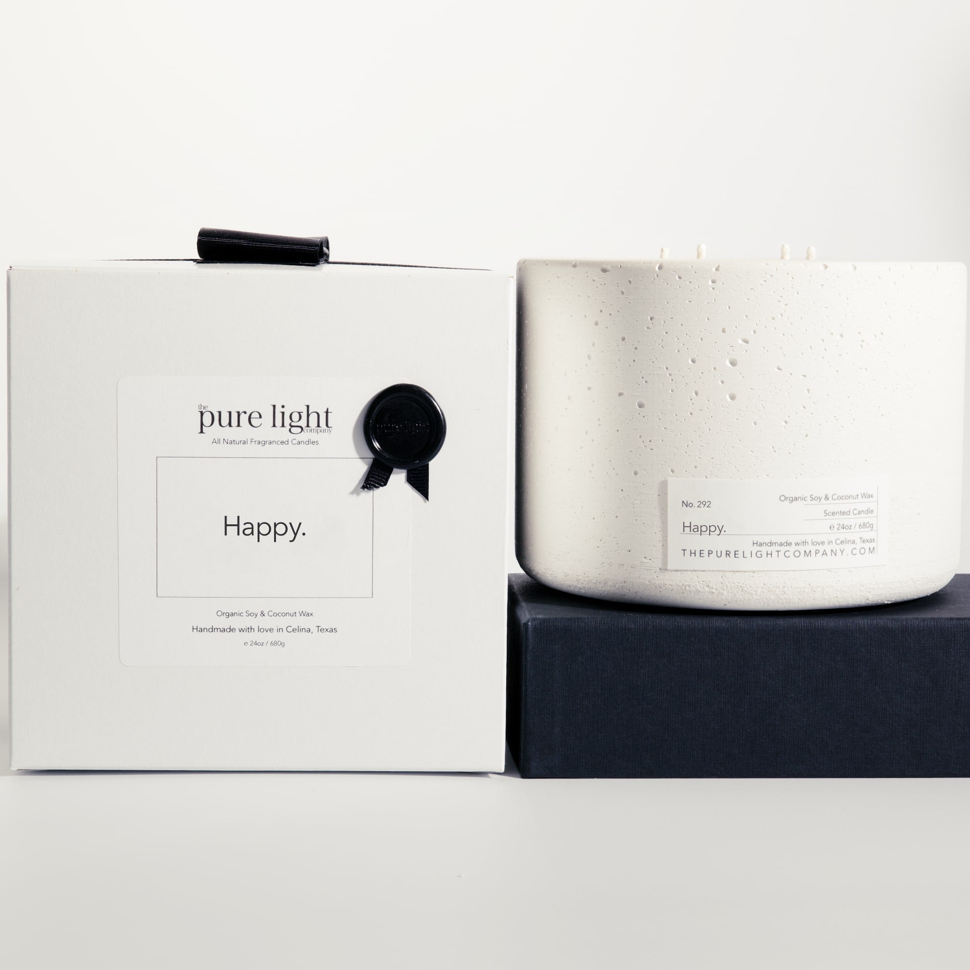 Extra large Happy white concrete candle on a prop beside a gift box with ribbon and wax seal by The Pure Light Company.