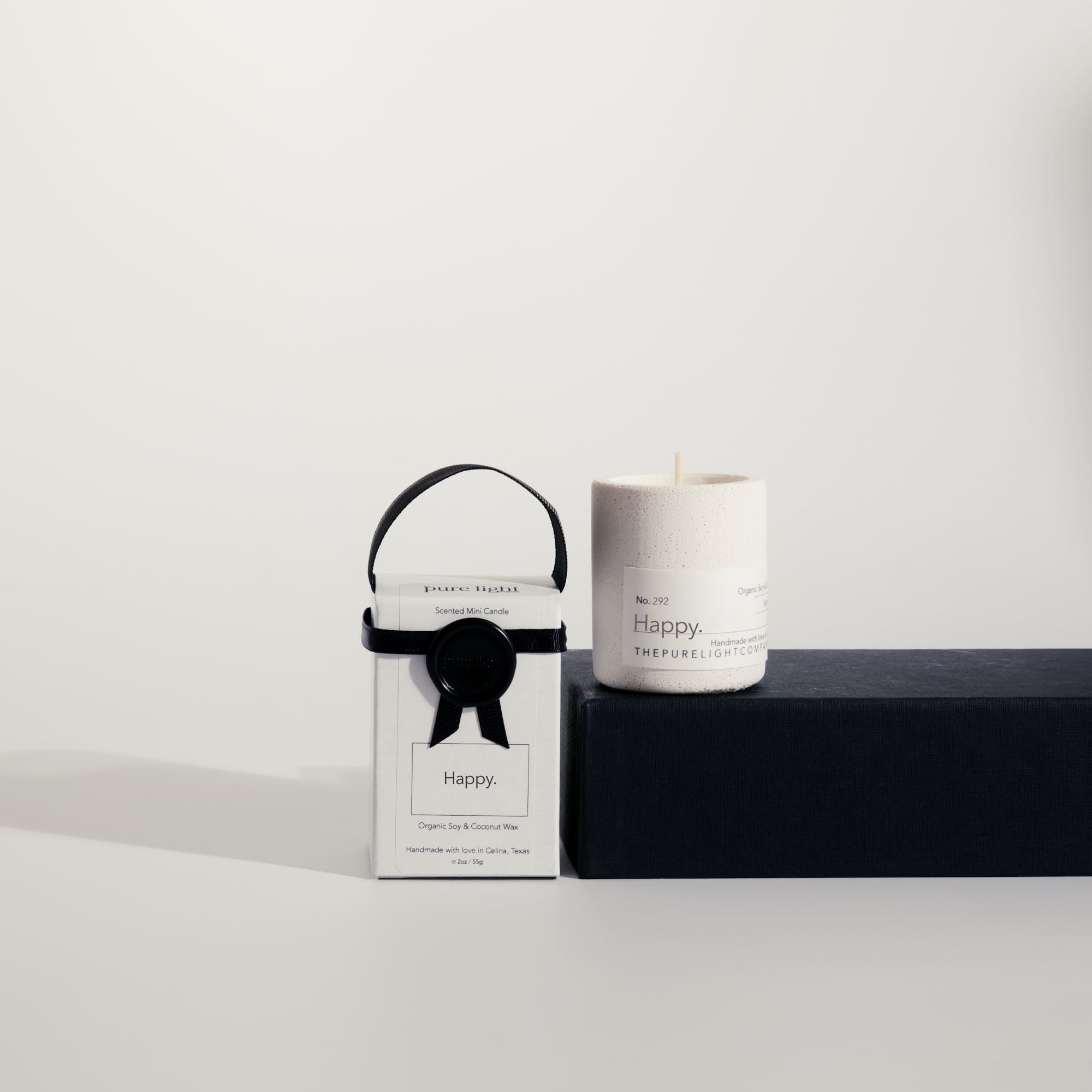 Mini Happy concrete candle on a prop beside a gift box with ribbon and wax seal by The Pure Light Company.