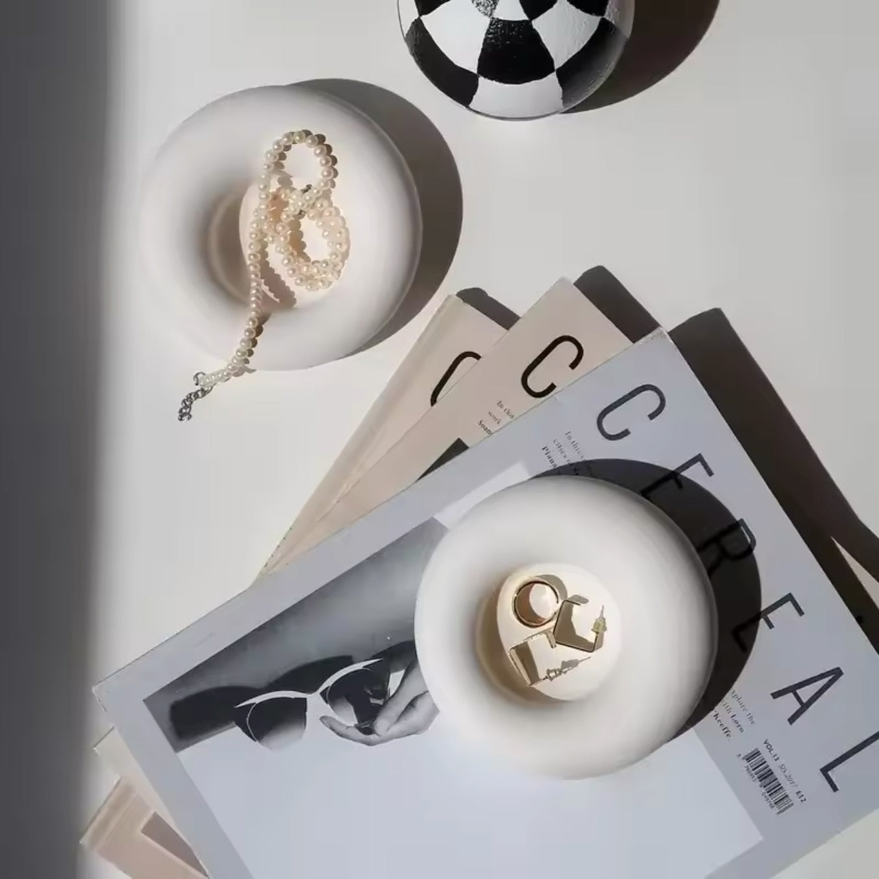 Two white concrete trinket dishes with 'the pure light company' branding on a magazine