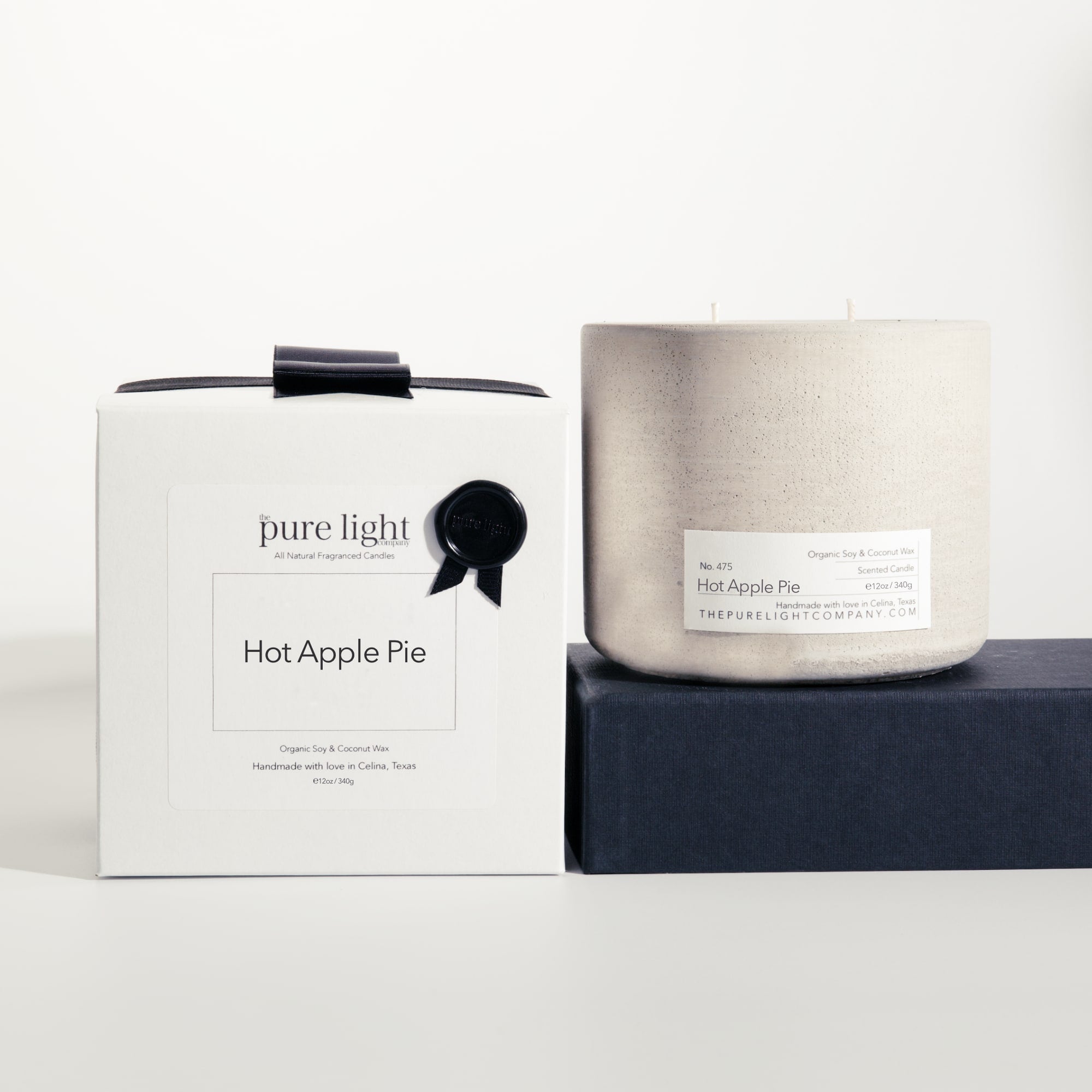 Large Hot Apple Pie gray concrete candle on a prop beside a gift box with ribbon and wax seal by The Pure Light Company.