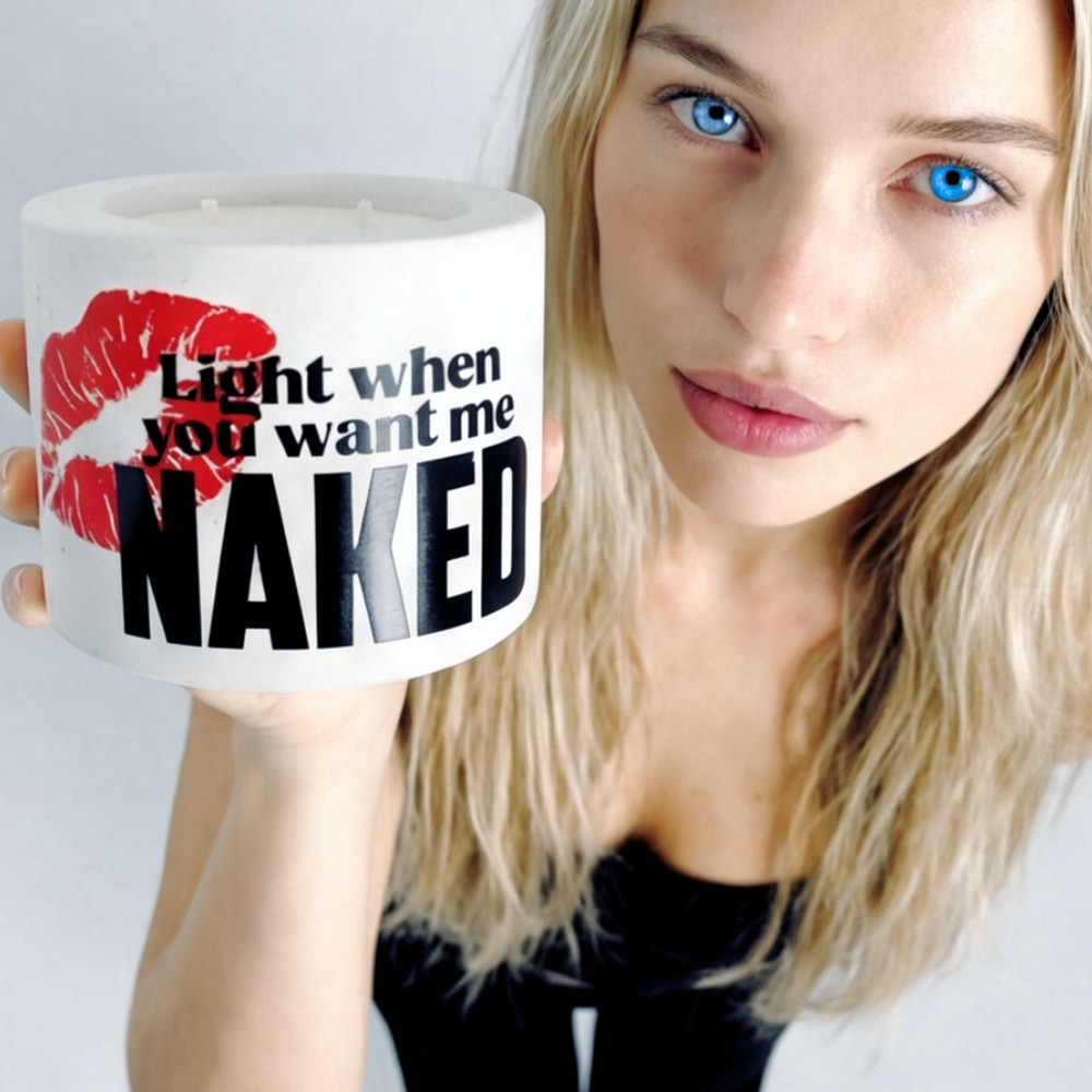 A lady with blonde hair and blue eyes is holding a candle with text and a red lipstick mark on a white concrete jar.