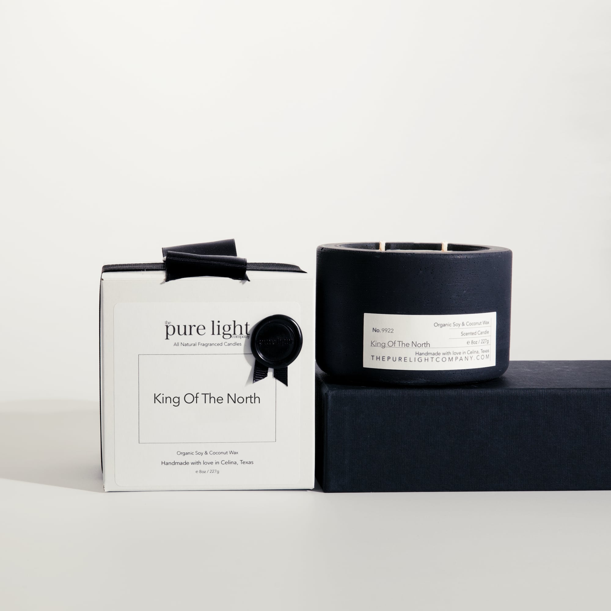 Medium King Of The North black concrete candle on a prop beside a gift box with ribbon and wax seal by The Pure Light Company.
