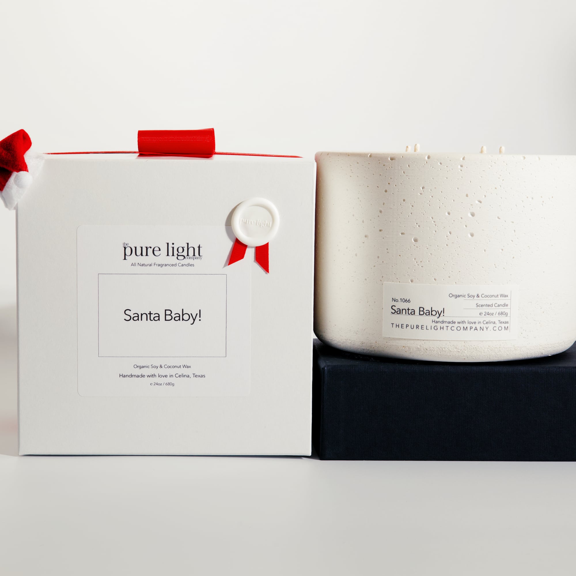 Extra Large Santa Baby! white concrete candle on a prop beside a gift box with ribbon and wax seal by The Pure Light Company.