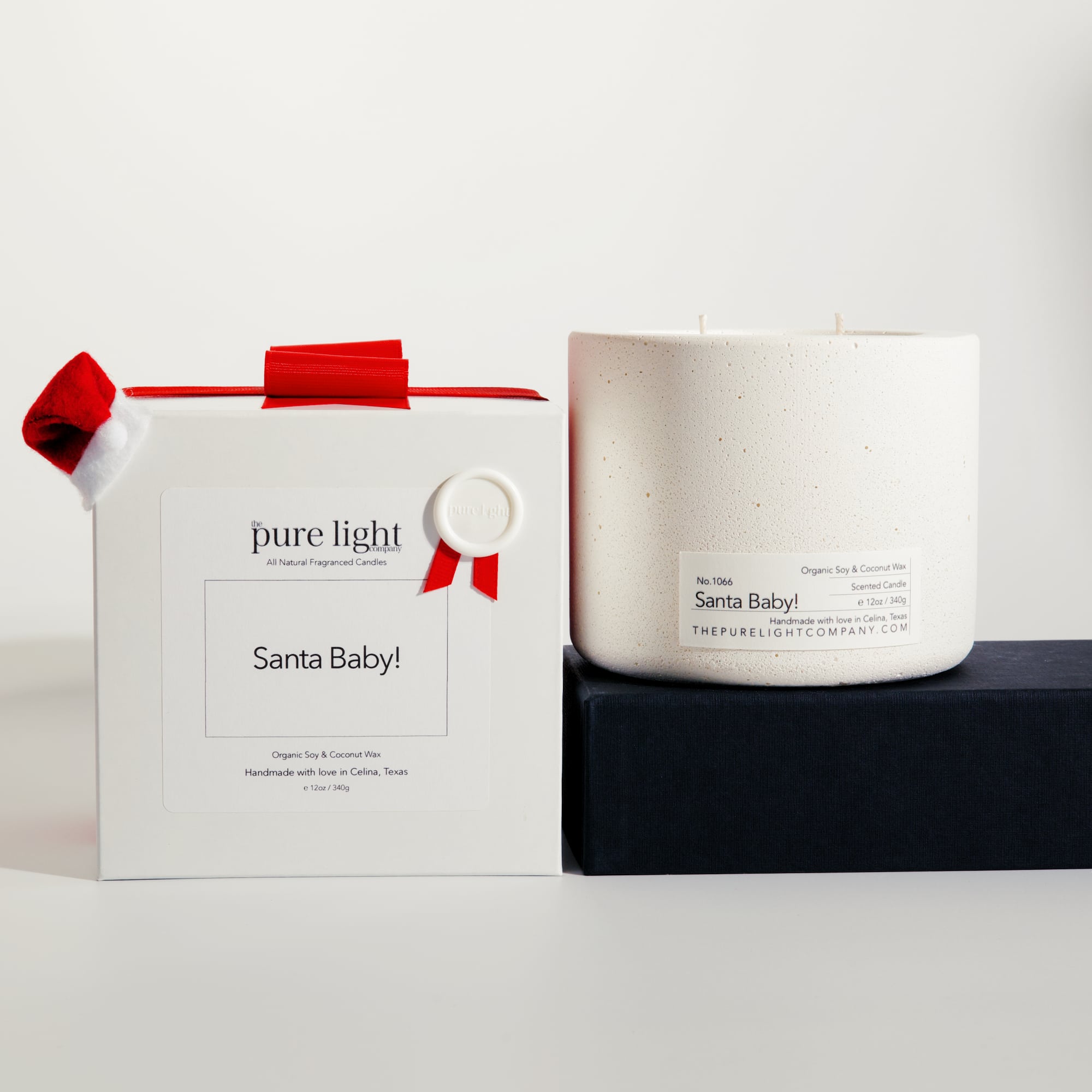 Large Santa Baby! white concrete candle on a prop beside a gift box with ribbon and wax seal by The Pure Light Company
