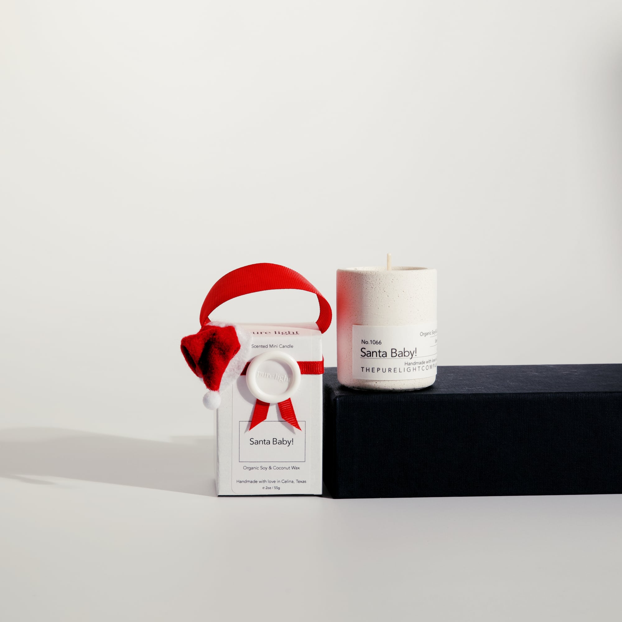 Mini Santa Baby! white concrete candle on a prop beside a gift box with ribbon and wax seal by The Pure Light Company.