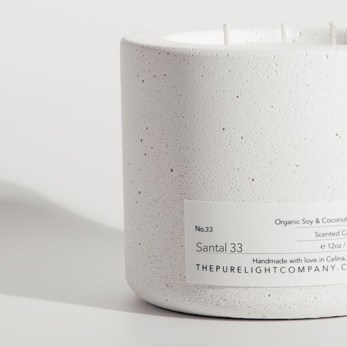 A close up of a white concrete candle jar labeled 'Santal 33' by 'The Pure Light Company' set against a clean white background.