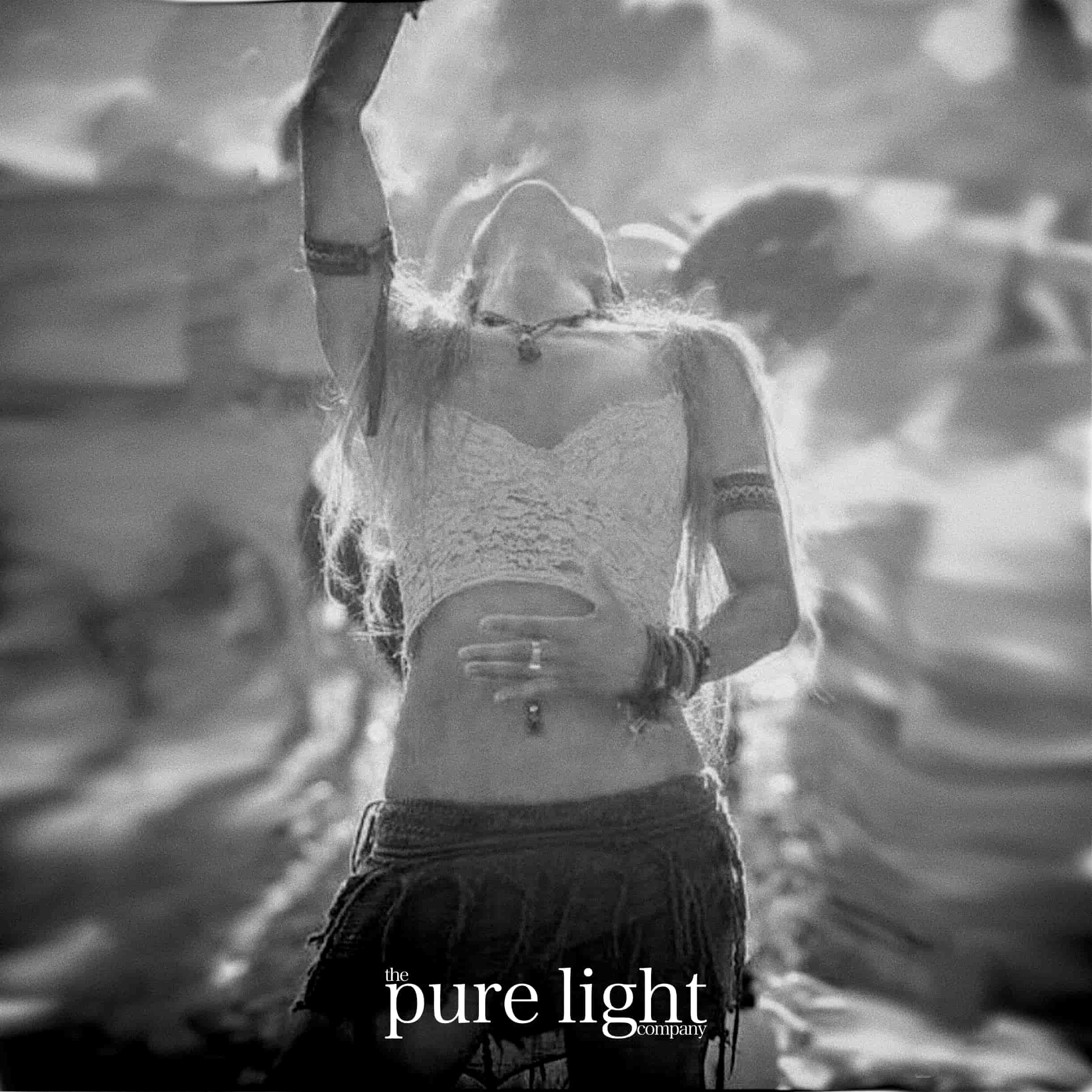 A black and white photograph of a woman with her head tilted back and arms raised, featuring The Pure Light Company logo at the bottom for the Sensuous Sandalwood products from The Pure Light Company all-natural fragranced candles and home fragrance items.