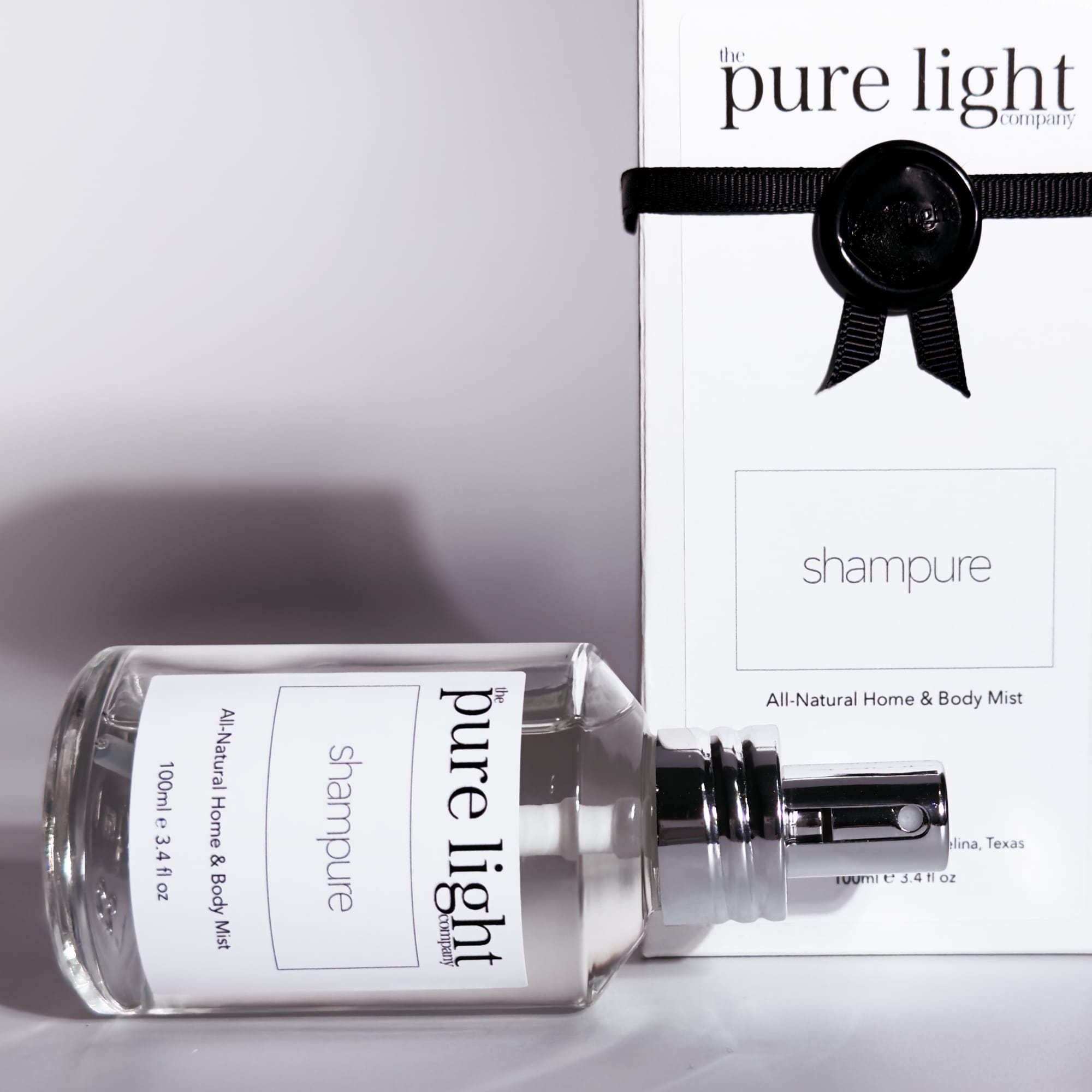 A clear bottle of SHAMPURE All-Natural Home & Body Mist 100ml laying on it's side with a ribboned box behind it