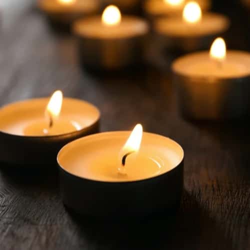 Multiple Aveda Shampure lit tealight candles with a yellow flame, placed on a dark surface, creating a warm, cozy atmosphere by The Pure Light Company.