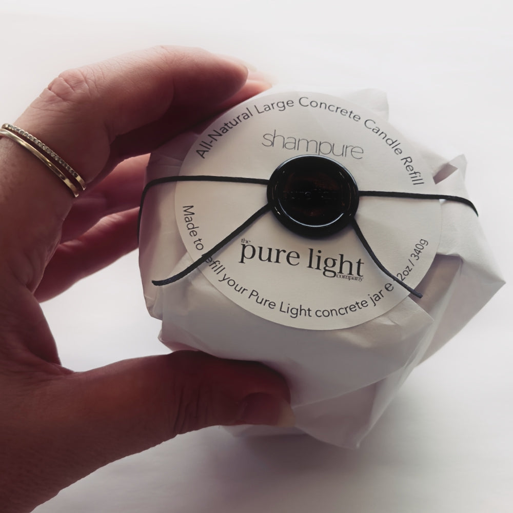 Hand holding a packaged refill wax candle with The Pure Light Company branding on a white background.