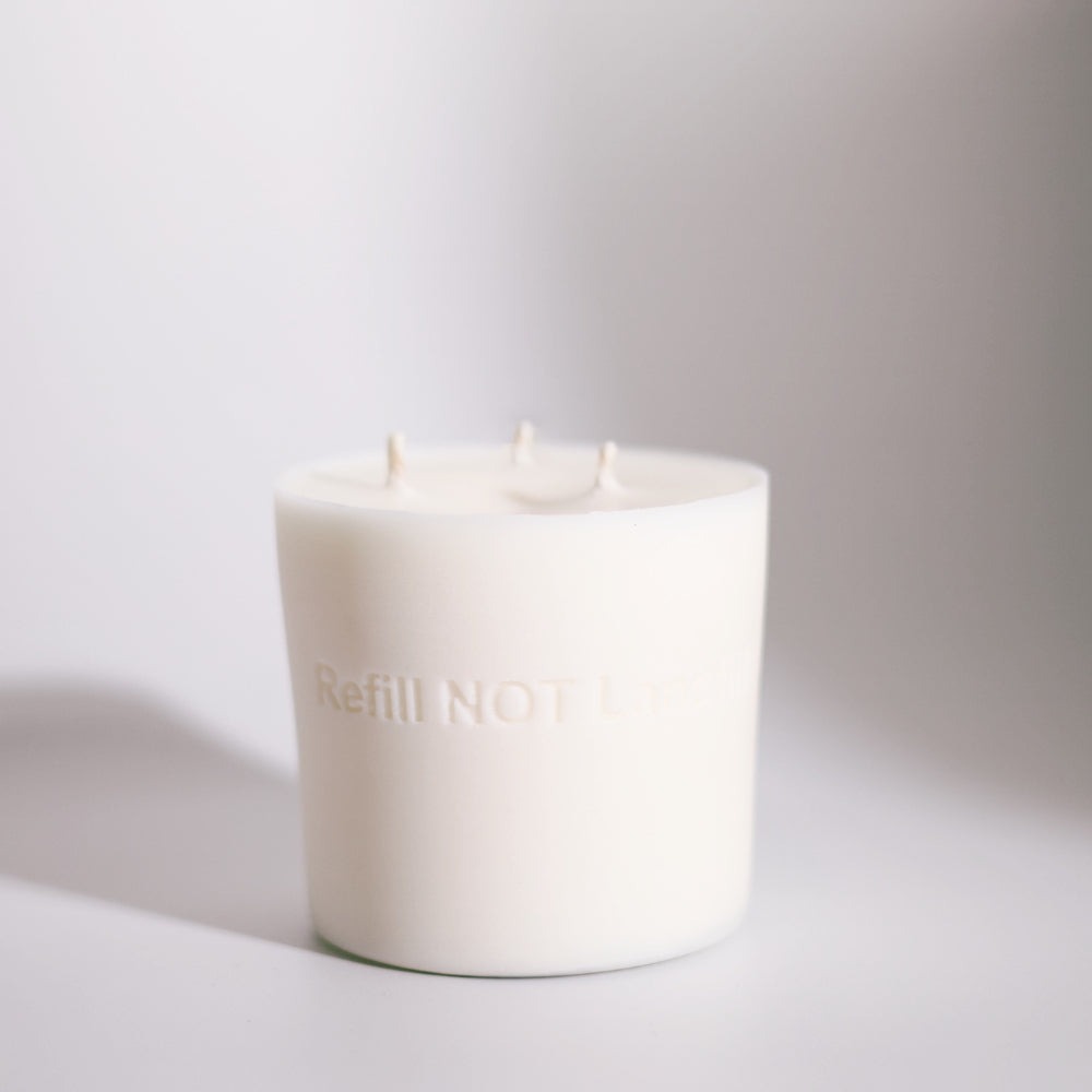 White candle with 'Refill Now' text on a light gray background by The Pure Light Company.